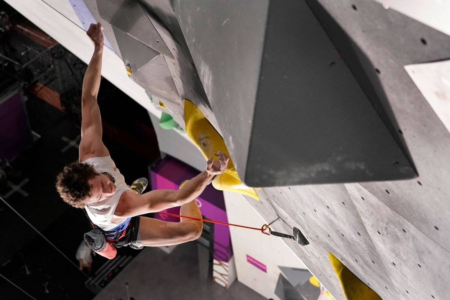 Climbing 桌布 壁紙 — 一名男性攀岩者懸掛在室內抱石牆的半空中，緊緊抓住一個黃色把手，神情專注。