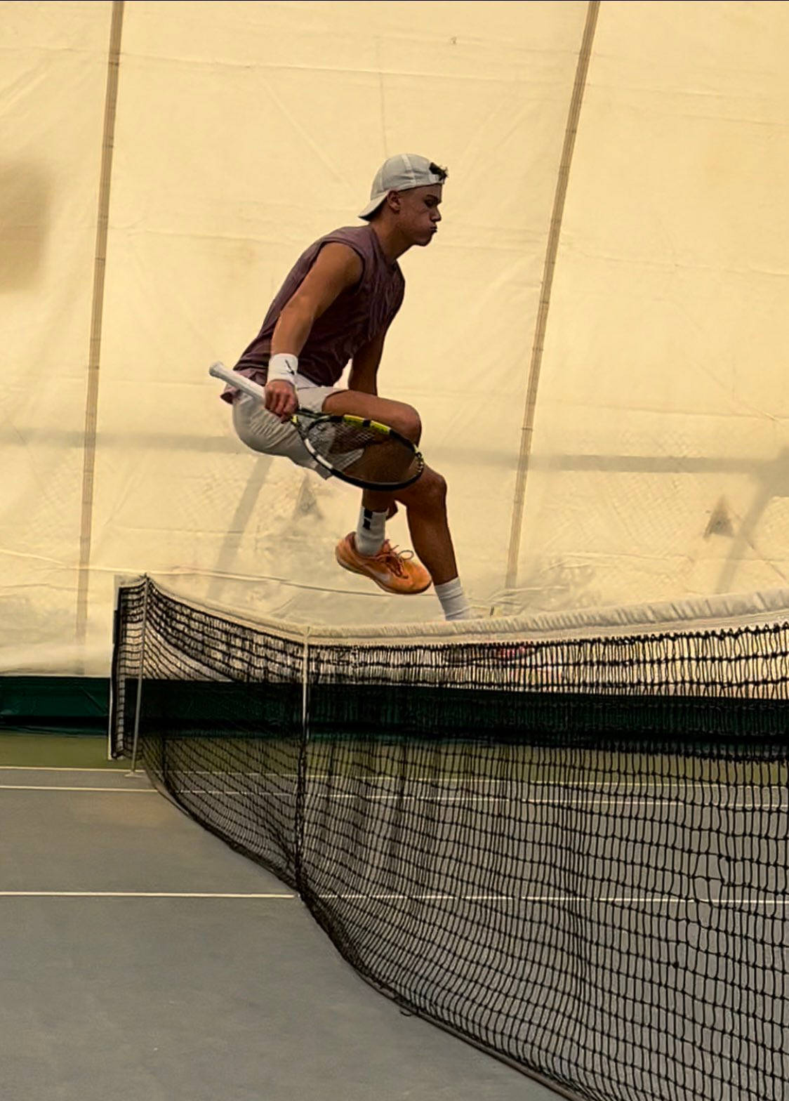 Tennis 桌布 壁紙 — 一名男性網球運動員在室內球場（米色牆壁、綠色地板）揮拍時跳過球網。