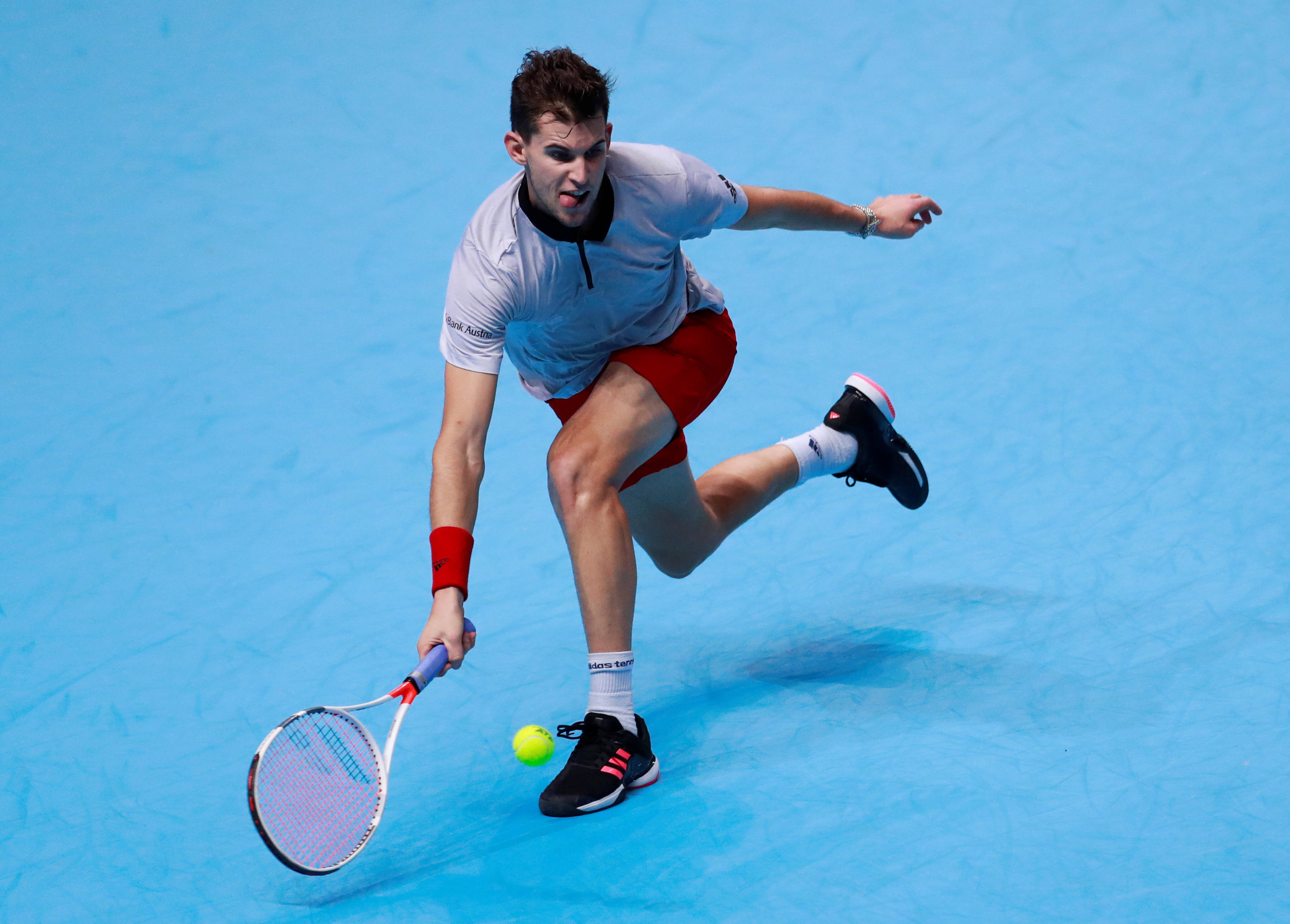 dominic thiem 桌布 壁紙 — 一名男性網球運動員在明亮的藍色球場上向前撲身，以高度專注擊打黃色網球。