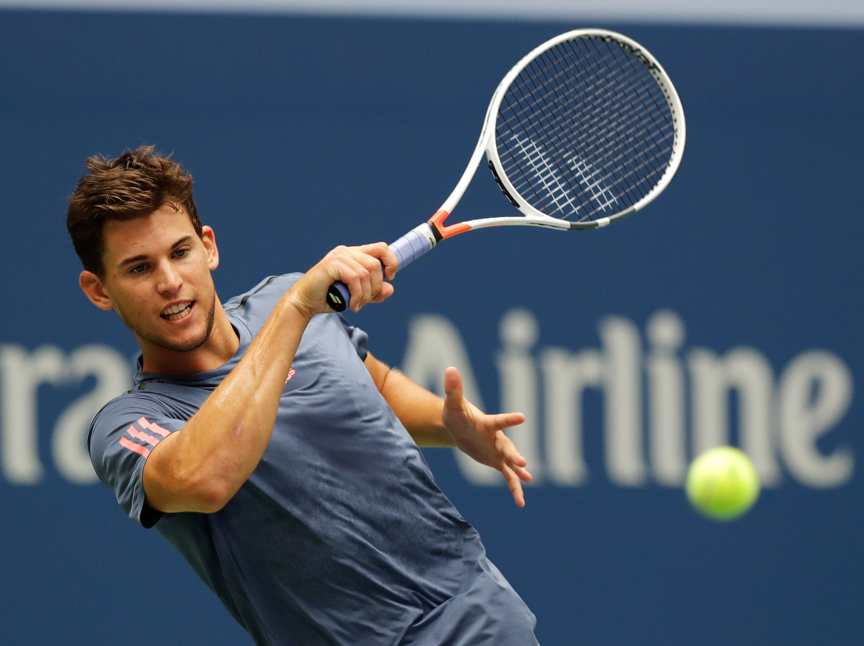 dominic thiem 桌布 壁紙 — 一名男性網球選手在揮拍中途，以強烈的專注力擊打一顆亮黃色的球，背景是藍色牆壁。