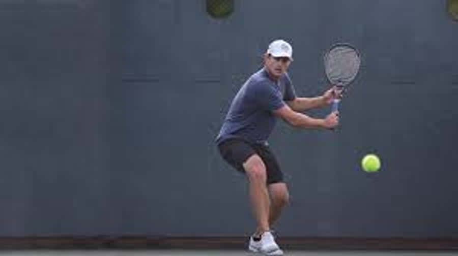 Tennis 桌布 壁紙 — 一名男性網球選手在揮拍中途，將明亮的黃色球擊向戶外球場的深灰色牆壁。