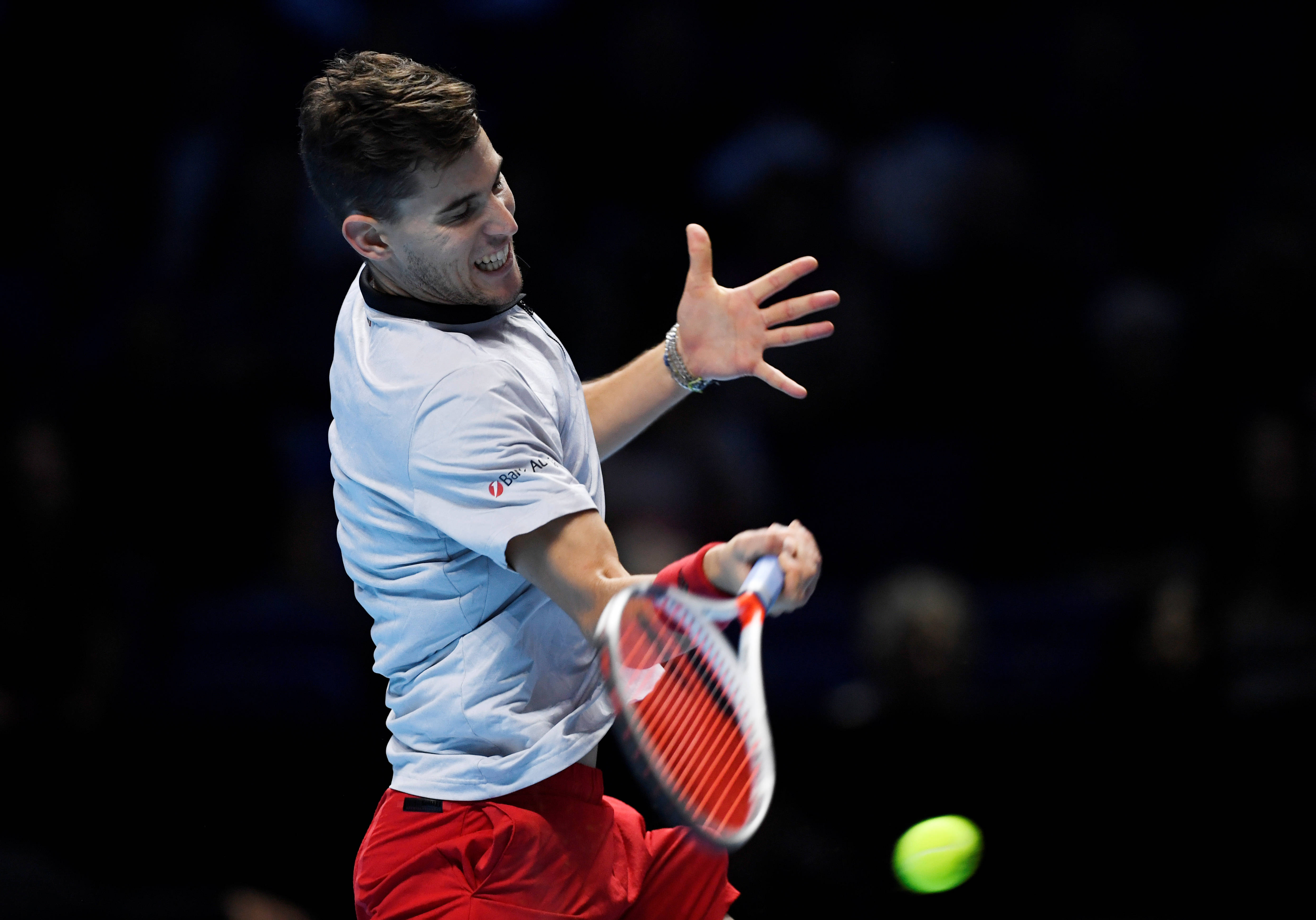 dominic thiem 桌布 壁紙 — 一名男性網球選手在揮拍中途，用紅白相間的球拍擊打一顆發光的綠色球，背景是黑暗模糊的。