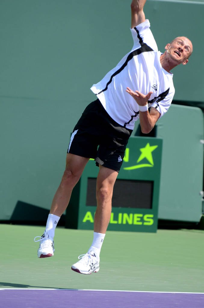 Tennis 桌布 壁紙 — 一名男性網球選手在明亮的日光下於綠色球場高高躍起，執行強力發球。