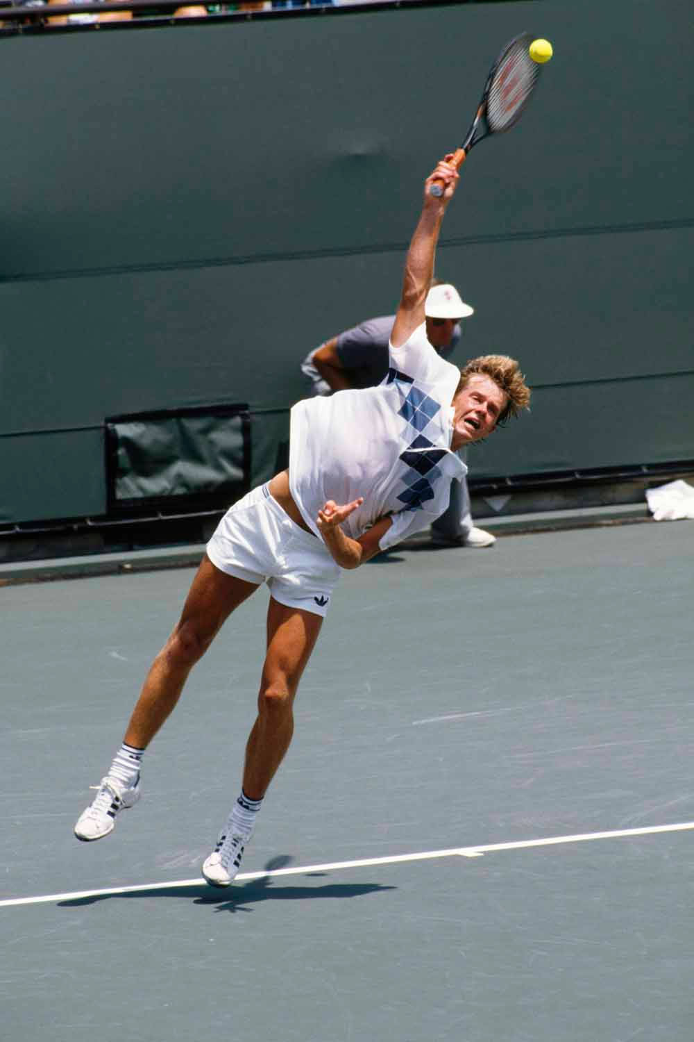 Tennis 桌布 壁紙 — 一名男性網球選手在空中高高躍起，揮動球拍擊打黃色網球，下方是綠色球場，上方是明亮的陽光。