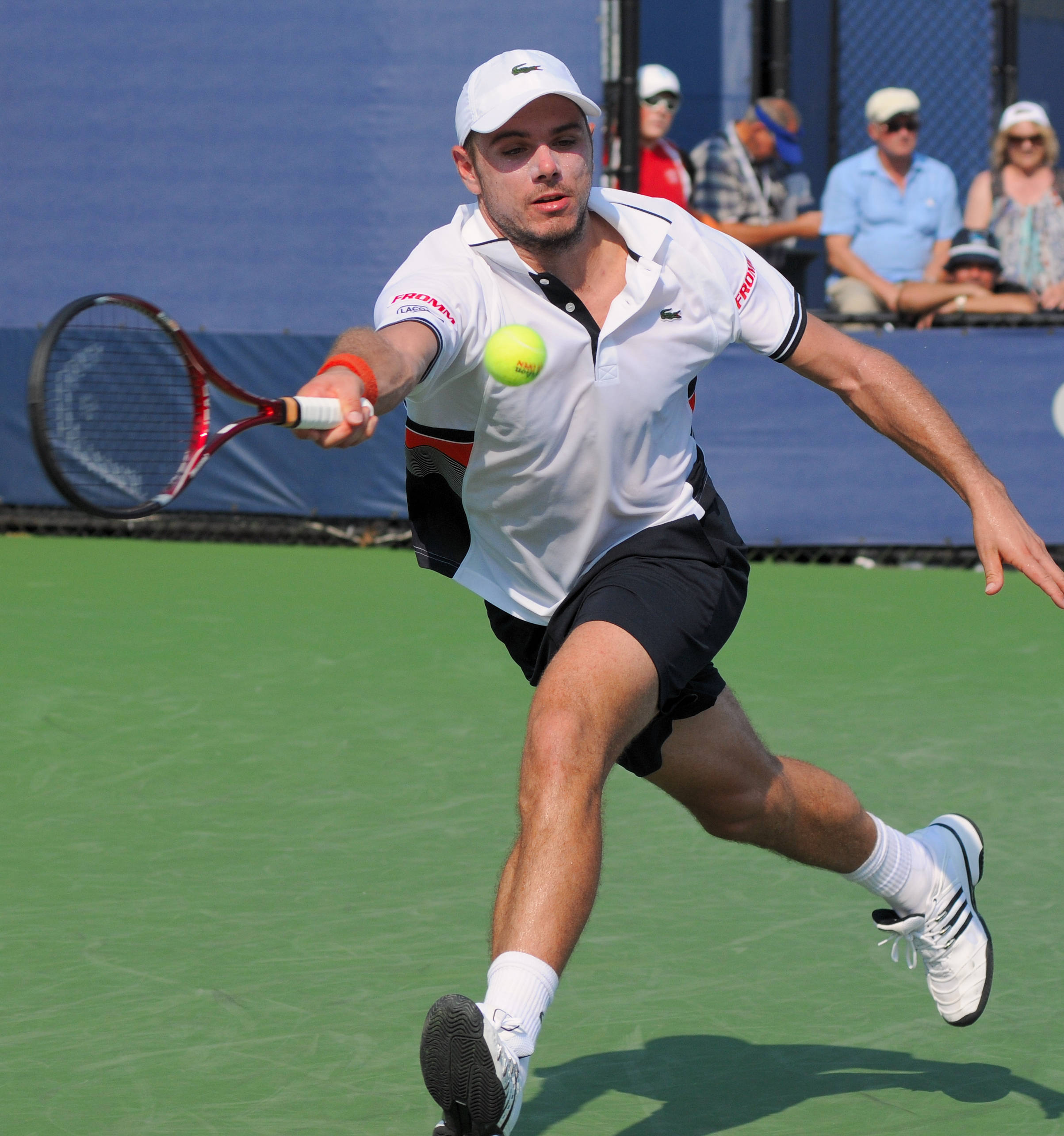 Tennis 桌布 壁紙 — 一名男性網球選手在綠色球場上向前猛衝，在明亮的日光下以高度專注擊打黃色球。