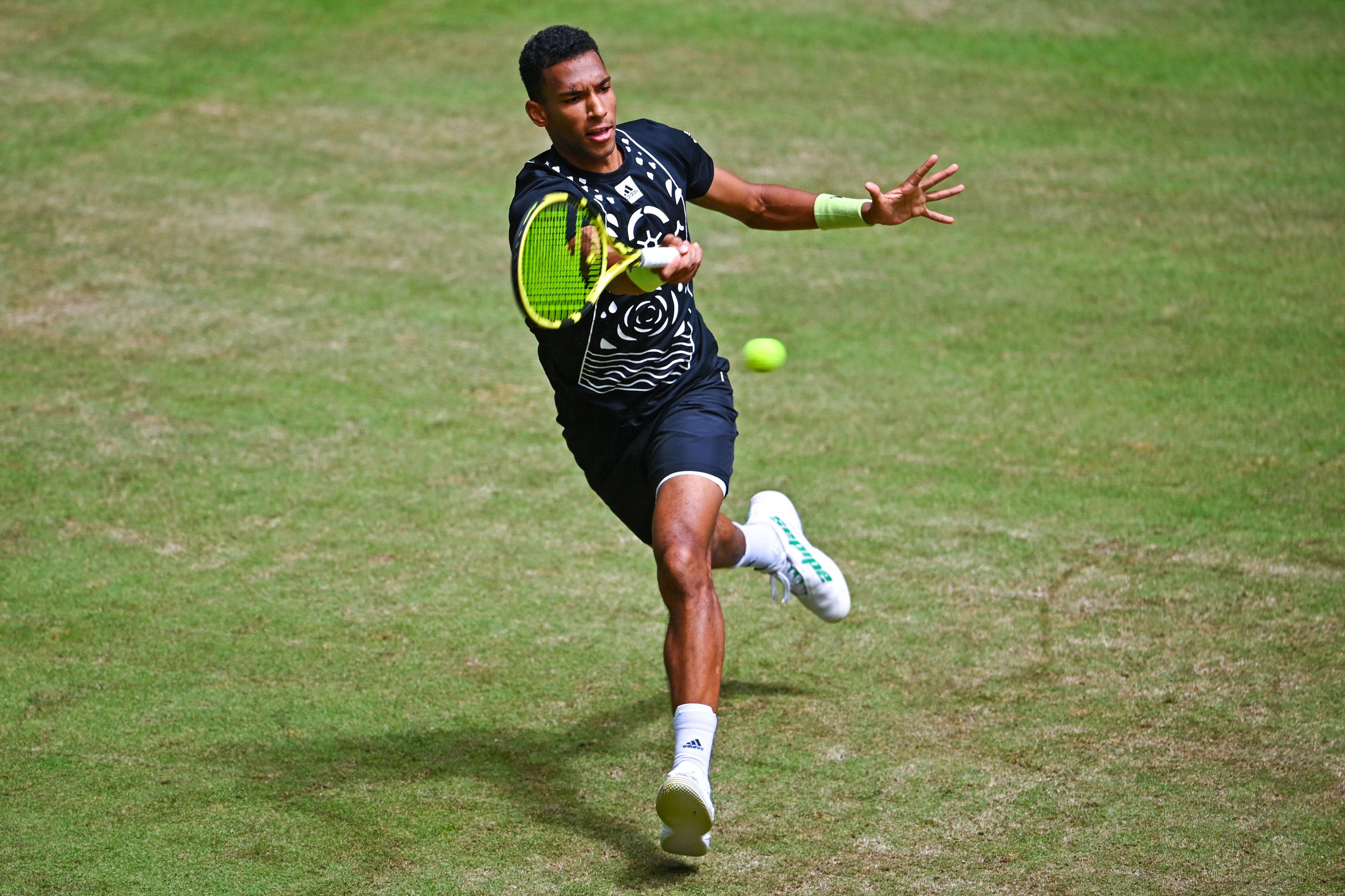 felix auger aliassime 桌布 壁紙 — 一名男性網球選手在草地場上向前撲出，用螢光綠色球拍擊打一個亮黃色的球。