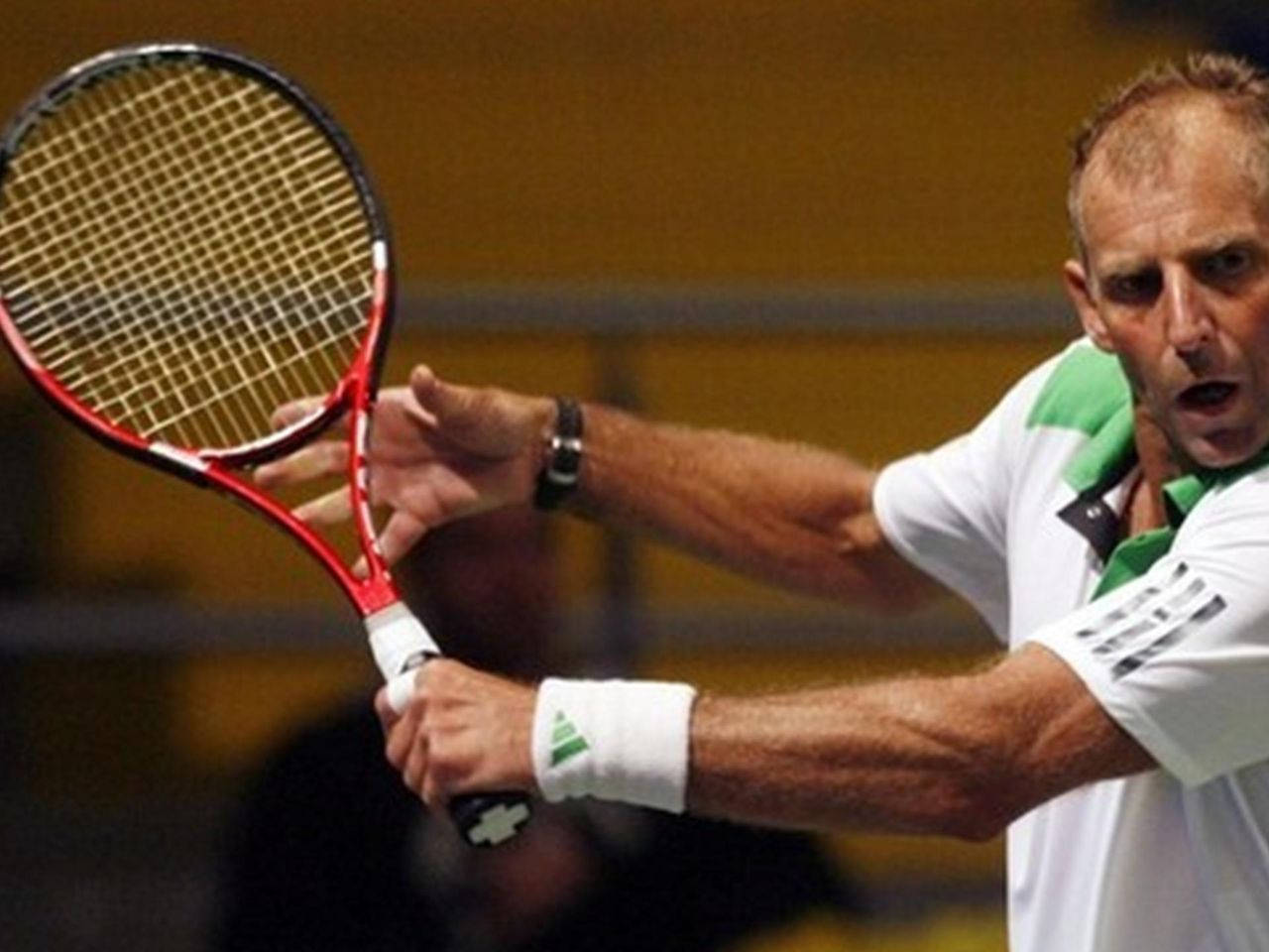 Tennis 桌布 壁紙 — 一名男性網球選手正處於揮拍動作中，專注地握著紅色球拍，背景是模糊的室內球場。
