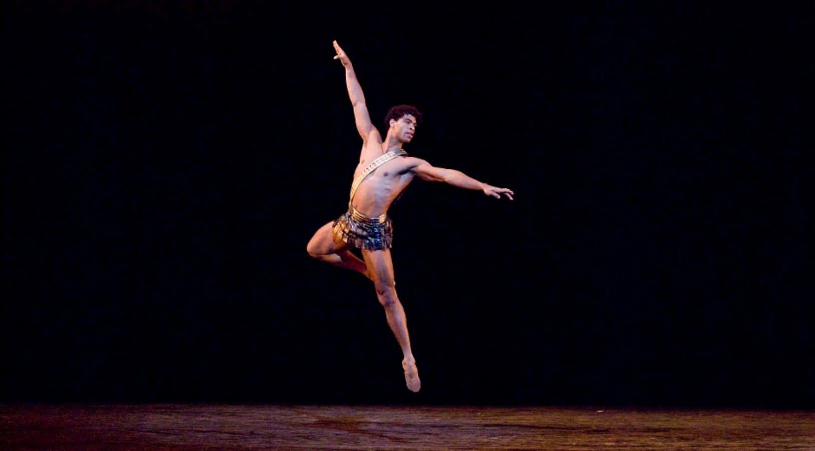 dancer 桌布 壁紙 — 一名男性芭蕾舞者在戲劇性的聚光燈下，在漆黑的舞台背景前優雅地騰空躍起。