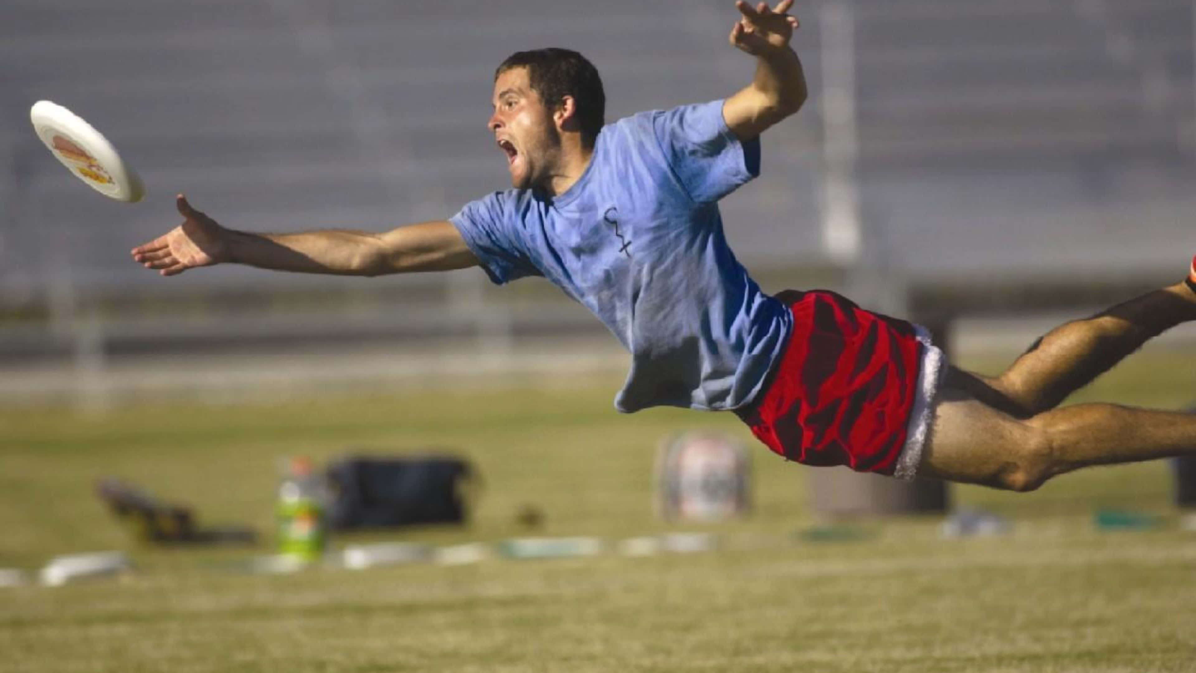 4K Frisbee 桌布 壁紙 — 一名男性運動員在草地上騰空飛撲，專注地伸手去接飛行的飛盤。