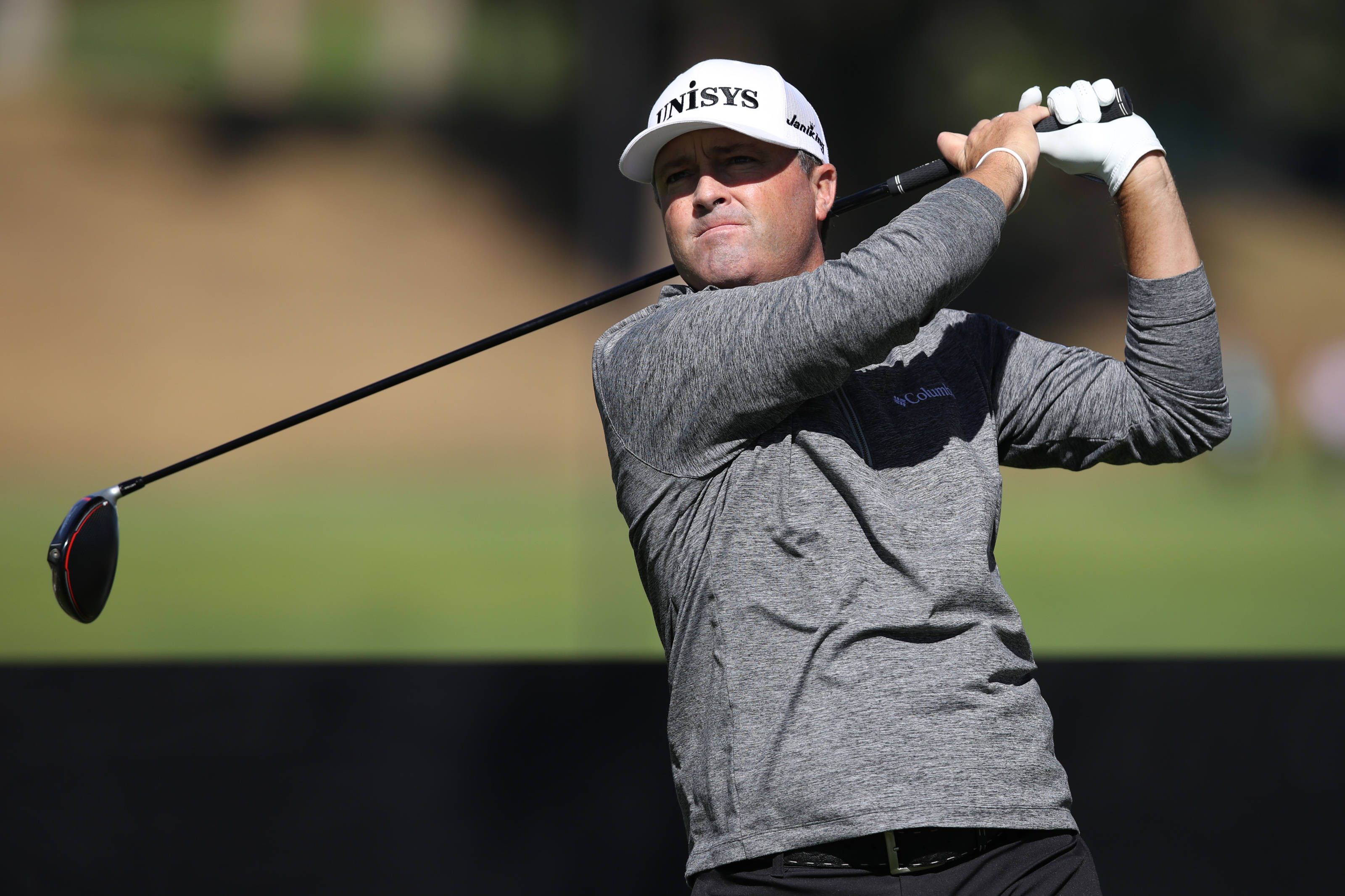 Ryan Palmer 桌布 壁紙 — 一名男性高爾夫球手在陽光普照的日子中揮桿，背景是模糊的綠色球道。