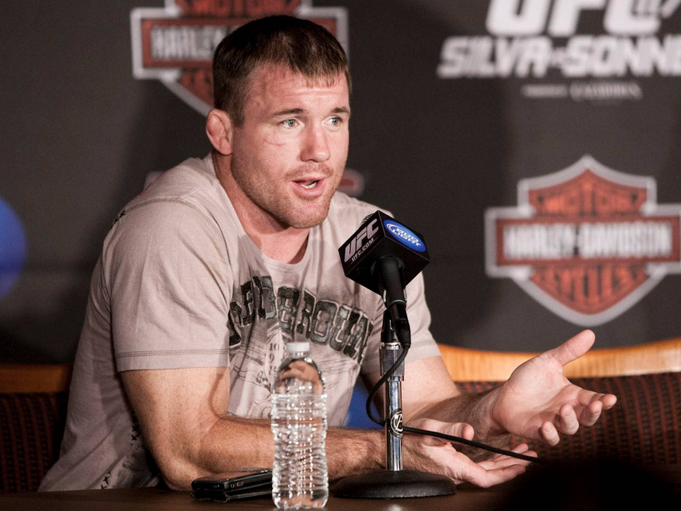 UFC 桌布 壁紙 — 一名男拳手在記者會上熱情地對著UFC麥克風發言，背後有Harley-Davidson品牌標誌。