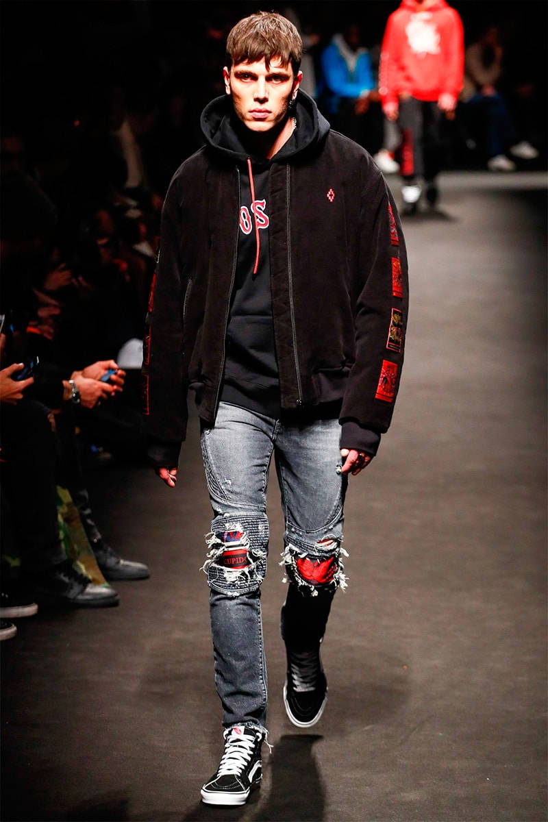 Fashion Model 桌布 壁紙 — 一名男模特兒穿著黑色連帽外套、破洞牛仔褲和黑色運動鞋，在明亮的舞台燈光下走秀。