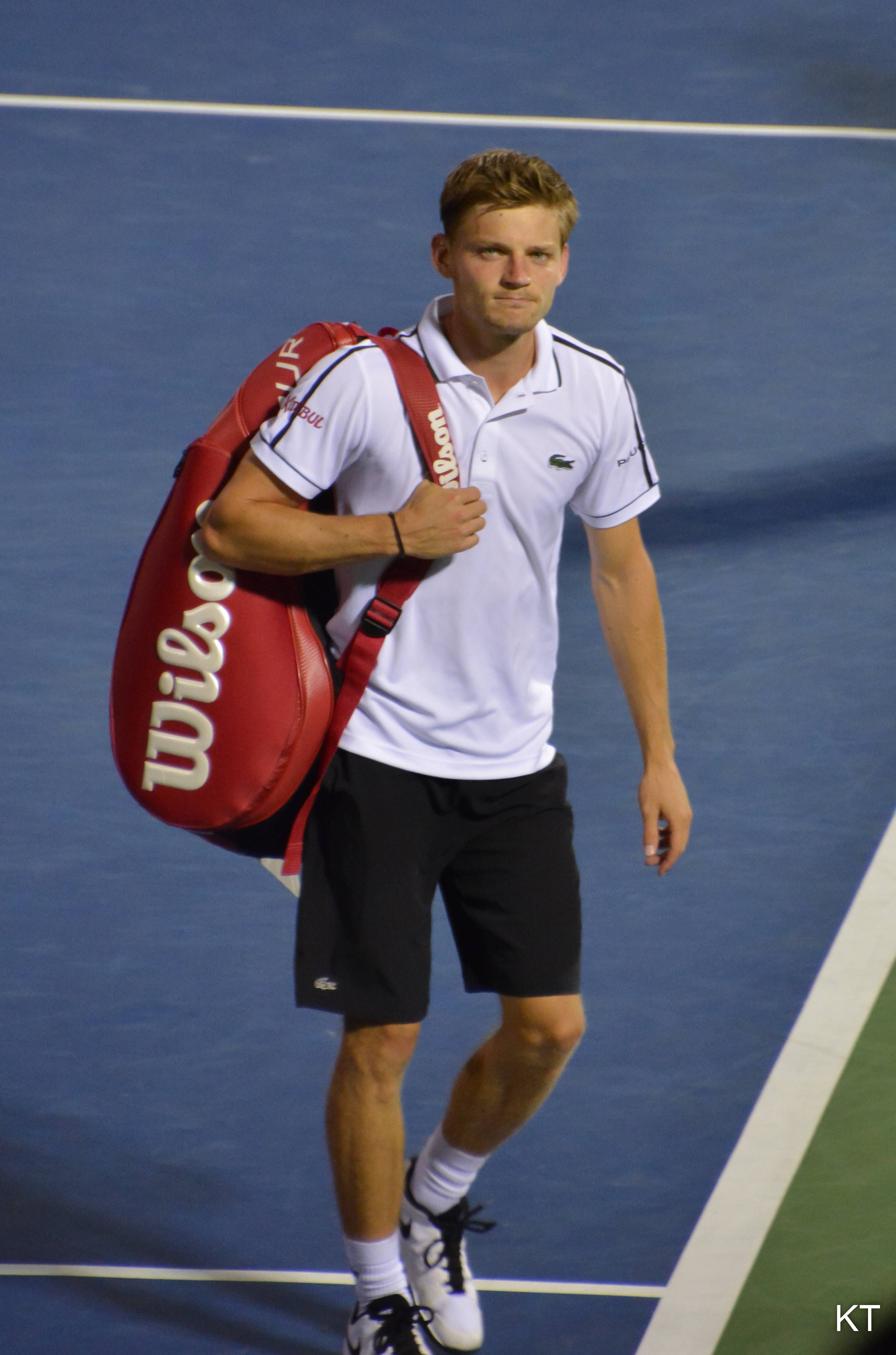 Tennis 桌布 壁紙 — 一名男網球運動員在體育場燈光下，拿著紅色Wilson袋，從藍色硬地球場走開。