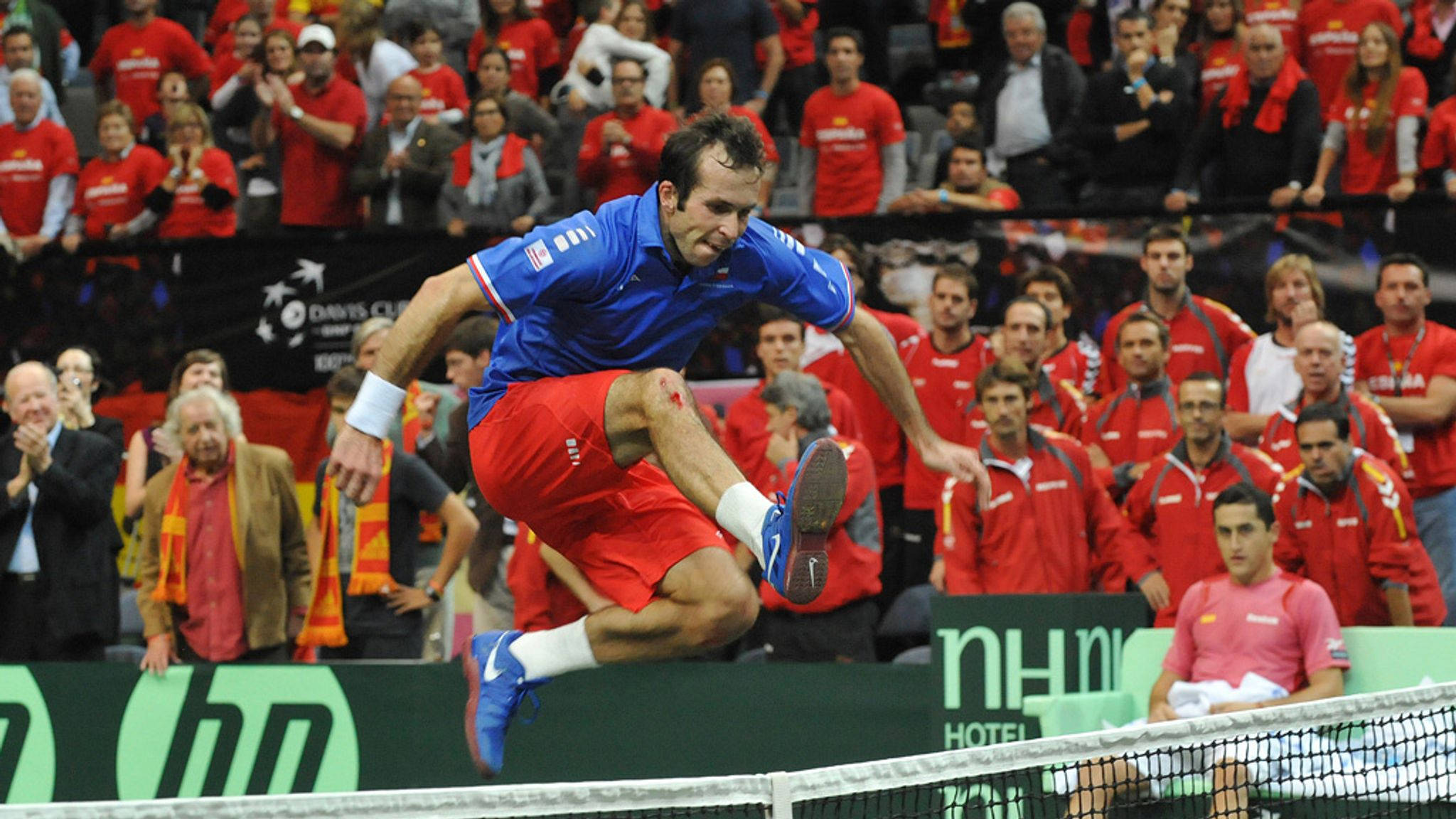 Tennis 桌布 壁紙 — 一名男網球選手在激烈的台維斯盃比賽中跳起，做出動態的正手揮拍。