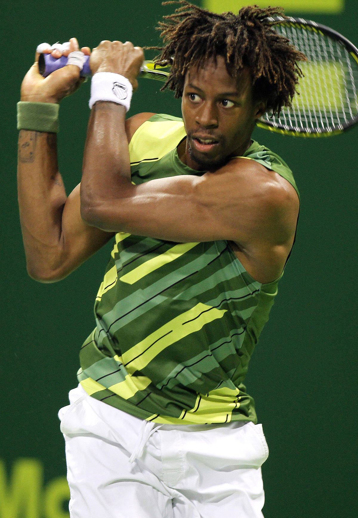 Tennis 桌布 壁紙 — 一名留有辮子頭的男性網球運動員在明亮的燈光下，在綠色球場上正手揮拍中。