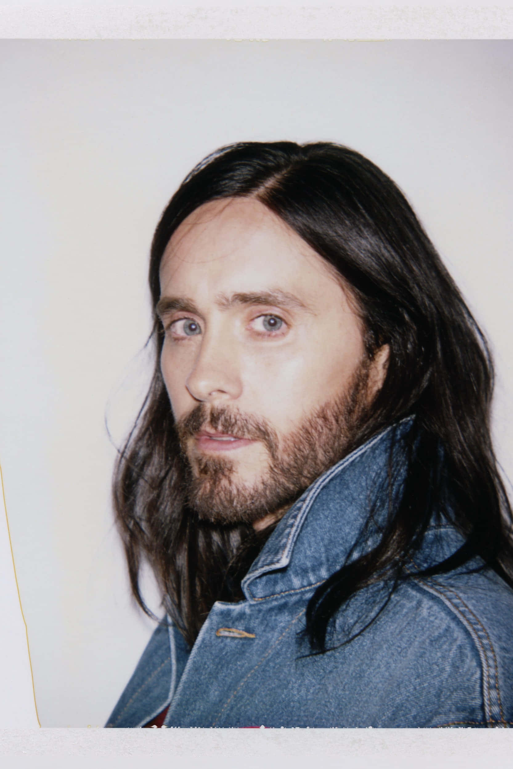 jared leto 桌布 壁紙 — 一名留著深色長髮和鬍鬚的男子，穿著牛仔外套，背景是純色米白色。