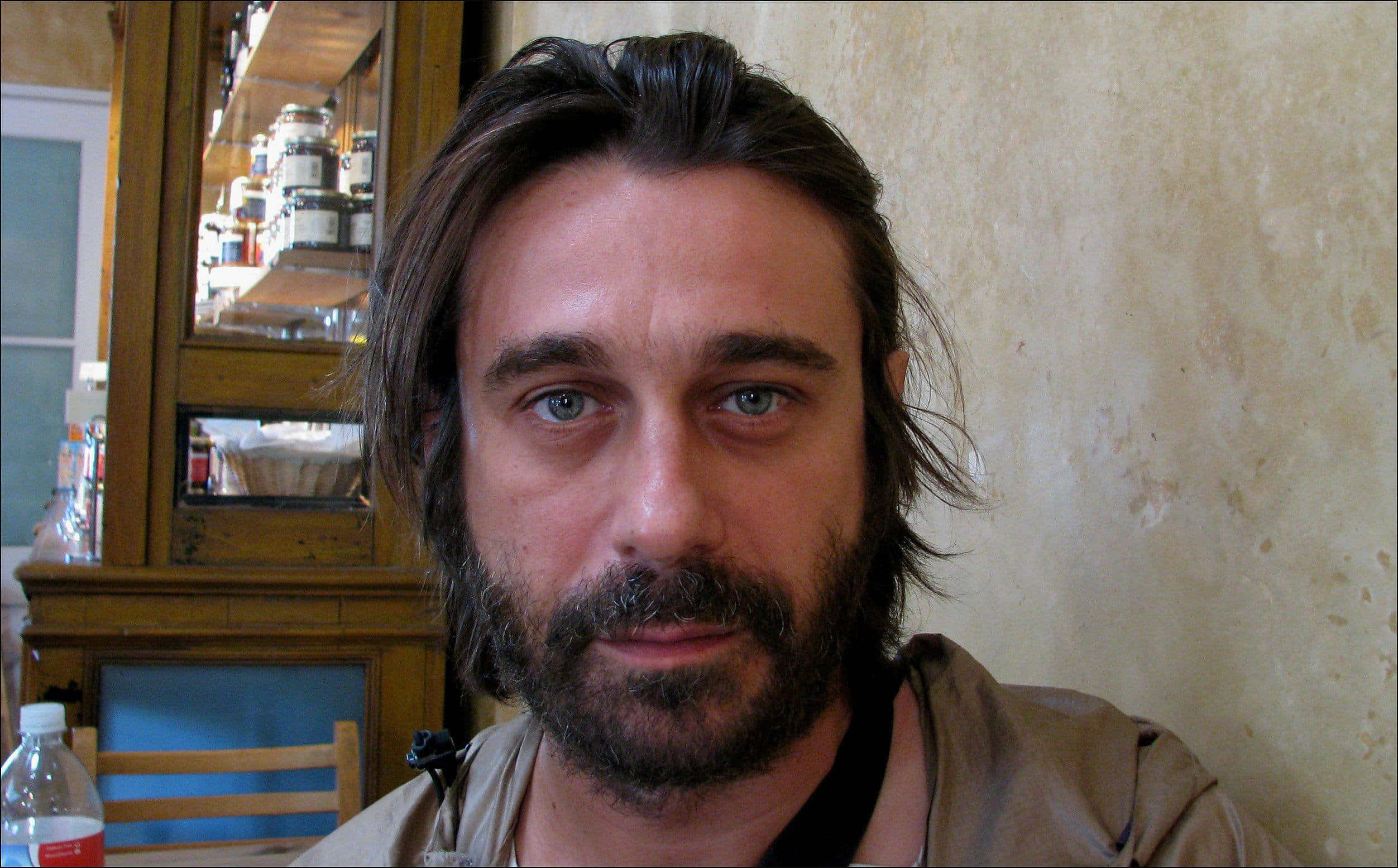 Jordi Mollà 桌布 壁紙 — 一名留著深色長髮和鬍鬚的男子在溫暖燈光的室內環境中直視鏡頭。