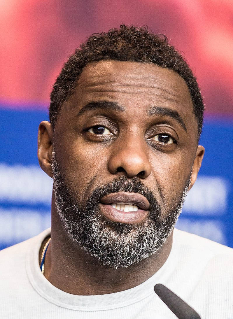 Celebrity 桌布 壁紙 — 一名留著灰白鬍鬚的男子在模糊的紅藍背景下對著麥克風說話的特寫肖像。