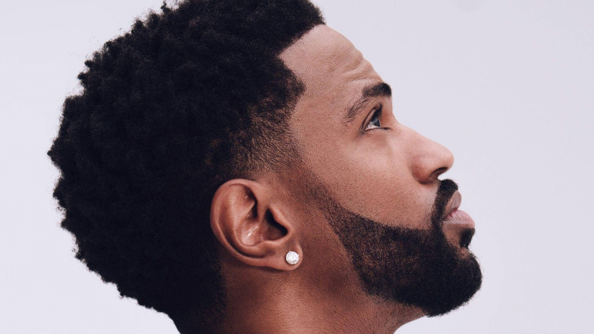 Big Sean 桌布 壁紙 — 一名留著紋理感爆炸頭和鬍鬚的男子，在純淺灰色背景前向上凝視。