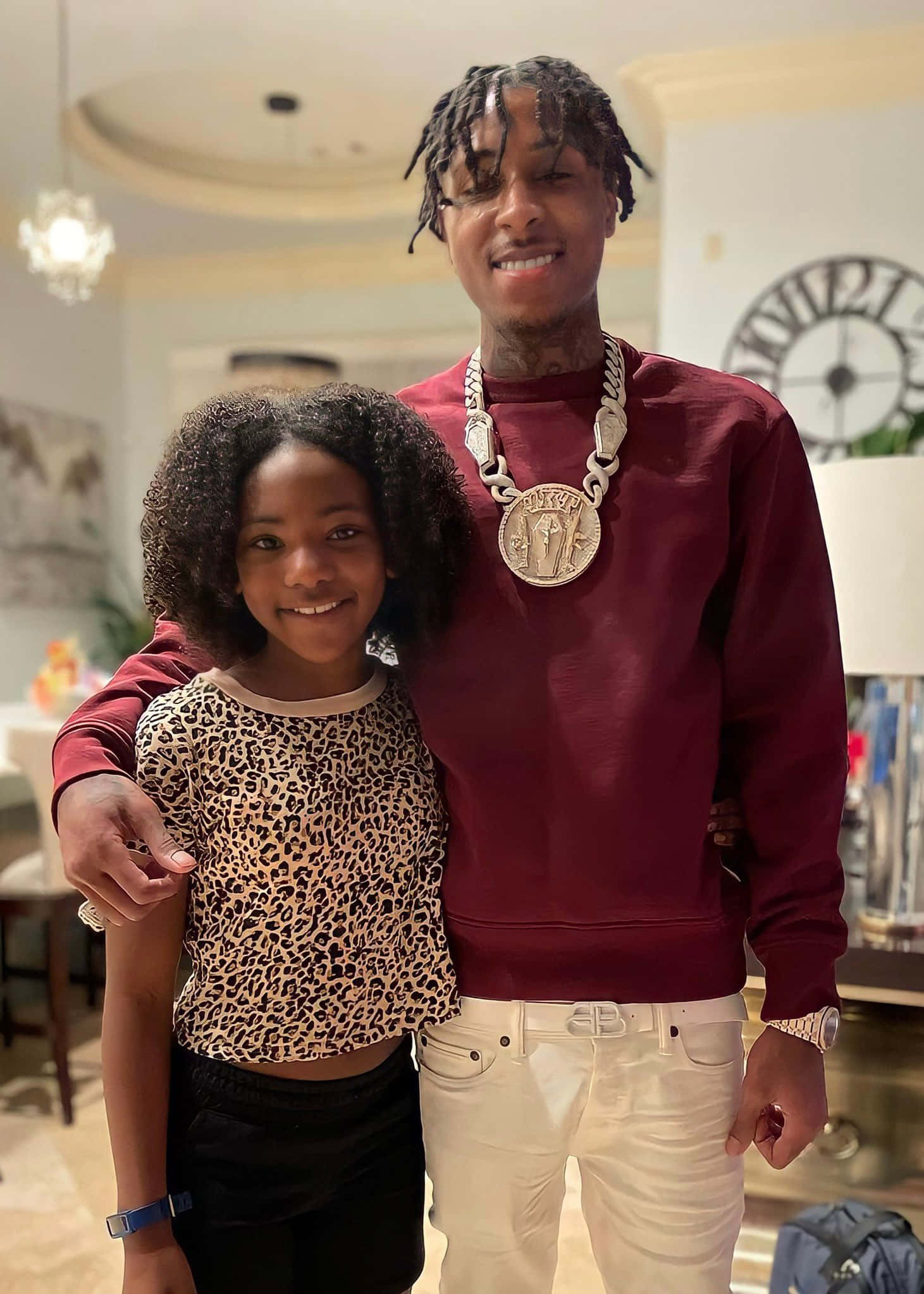 Youngboy 桌布 壁紙 — 一名留著辮子、戴著大鏈條的男子微笑著站在一名穿著豹紋上衣的年輕女孩旁邊，室內場景。