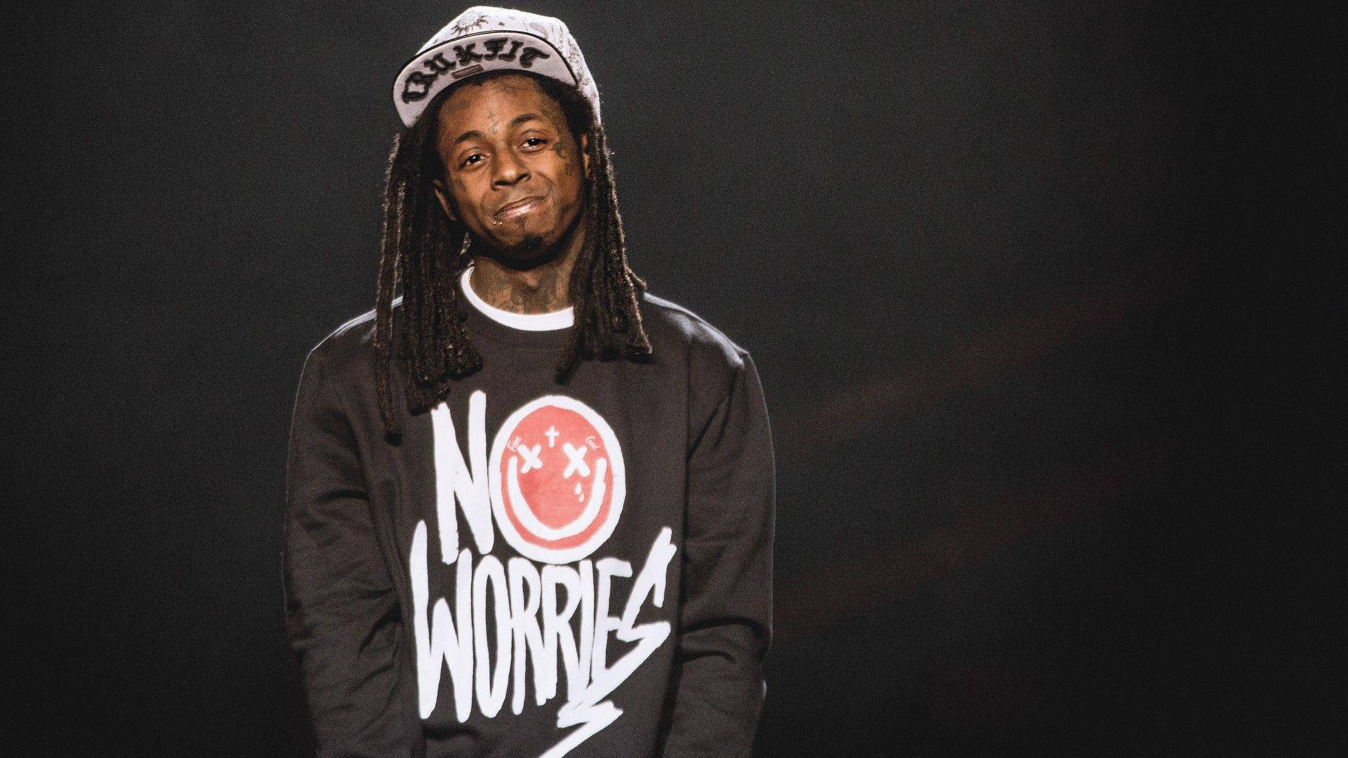 Lil Wayne 桌布 壁紙 — 一名留著辮子、戴著帽子的男士微笑著，身穿黑色衛衣，上面有紅色笑臉和白色「NO WORRIES」字樣。