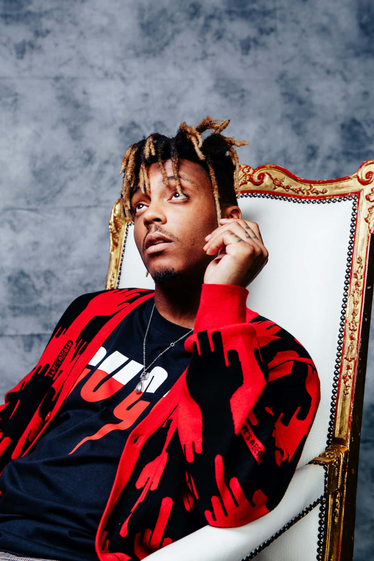留著辮子辮的男人坐在華麗椅子上，穿著紅黑圖案毛衣。 — Juice Wrld 壁紙