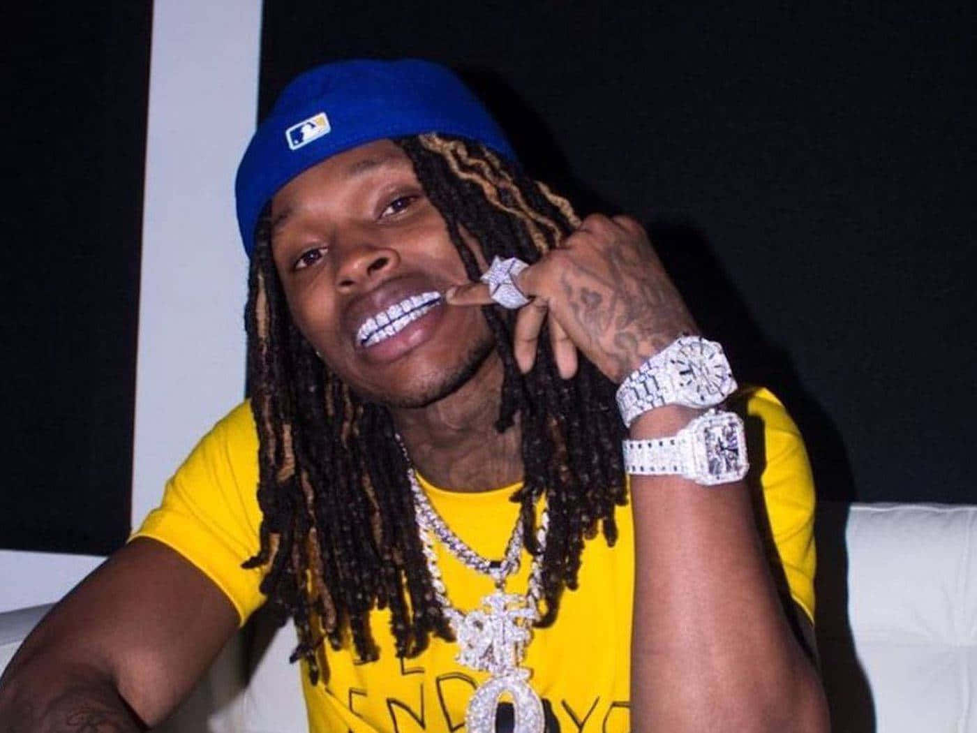 留著辮子頭、佩戴鑽石首飾的男子微笑著觸摸自己的牙齒。 — King Von 壁紙