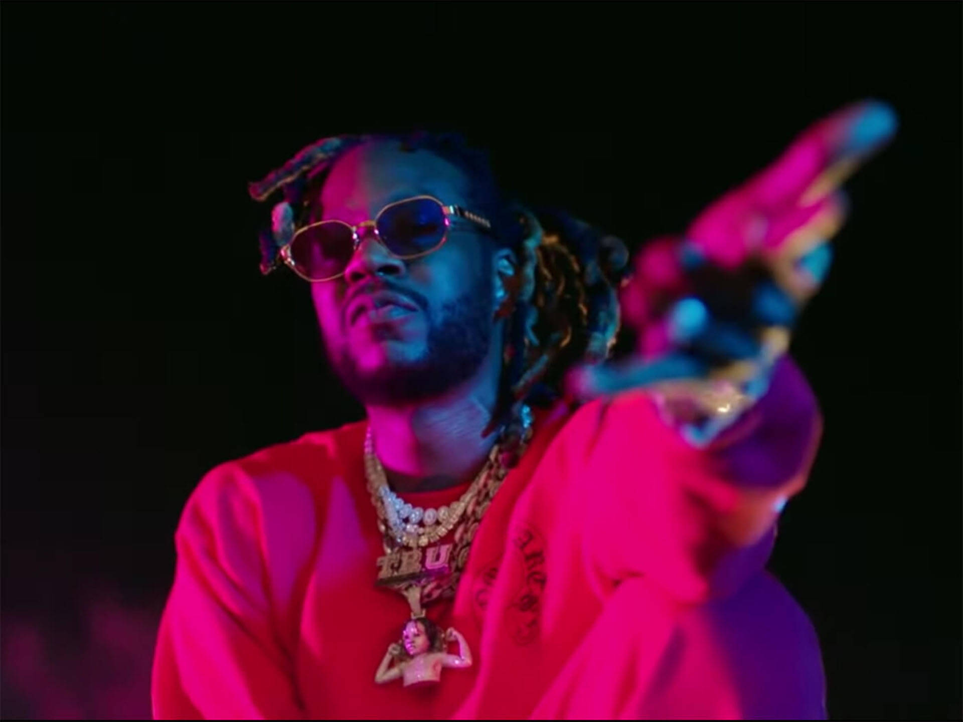 2 Chainz 桌布 壁紙 — 一名留著辮子頭、戴著太陽眼鏡的男子，在黑色背景的霓虹粉紅和藍色燈光下向前指。