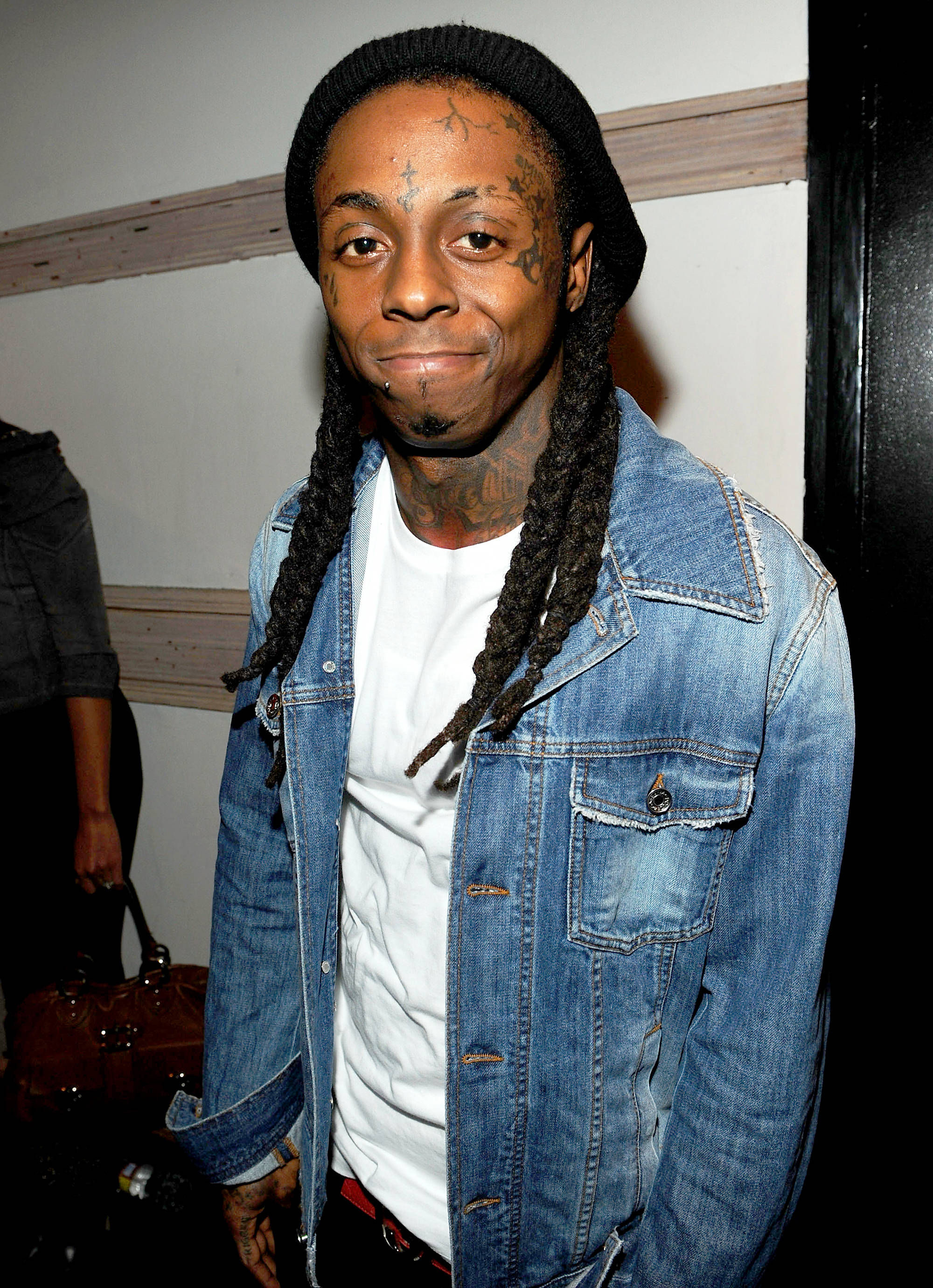Lil Wayne 桌布 壁紙 — 一名留著辮子頭和刺青的男子，在室內人造燈光下，身穿牛仔外套內搭白色T恤。