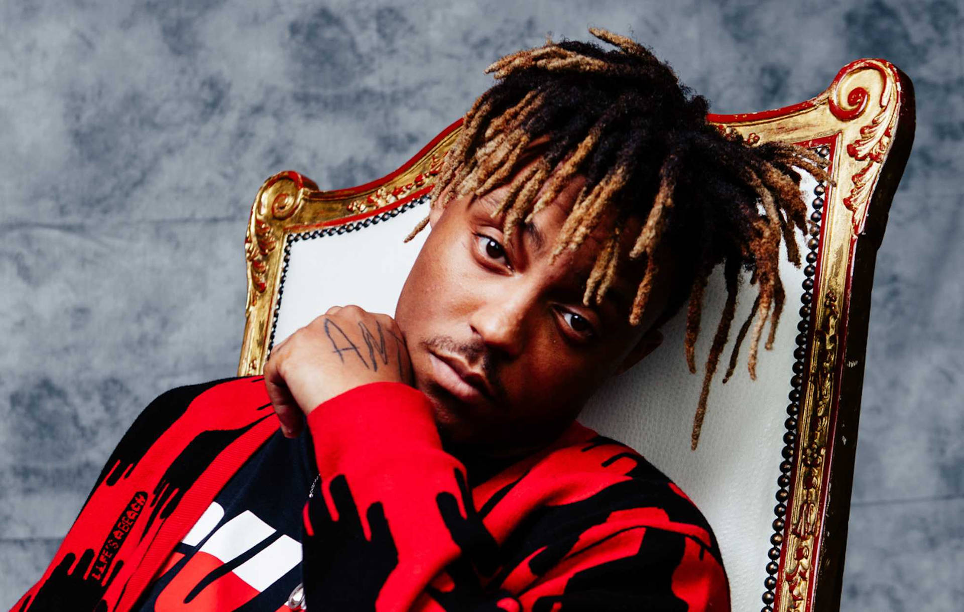 留著辮子頭的男人穿著紅黑連帽衫坐在華麗的金色椅子上。 — Juice Wrld 壁紙
