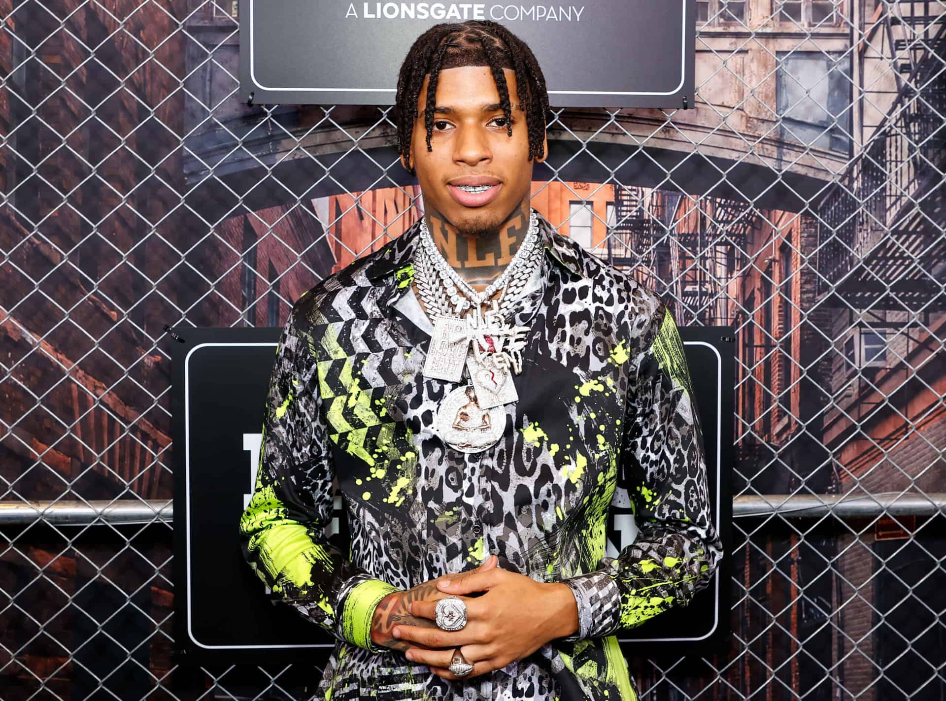 男子身穿大膽豹紋襯衫和銀飾，在鐵絲網圍欄後擺姿勢。 — NLE Choppa GIF 壁紙