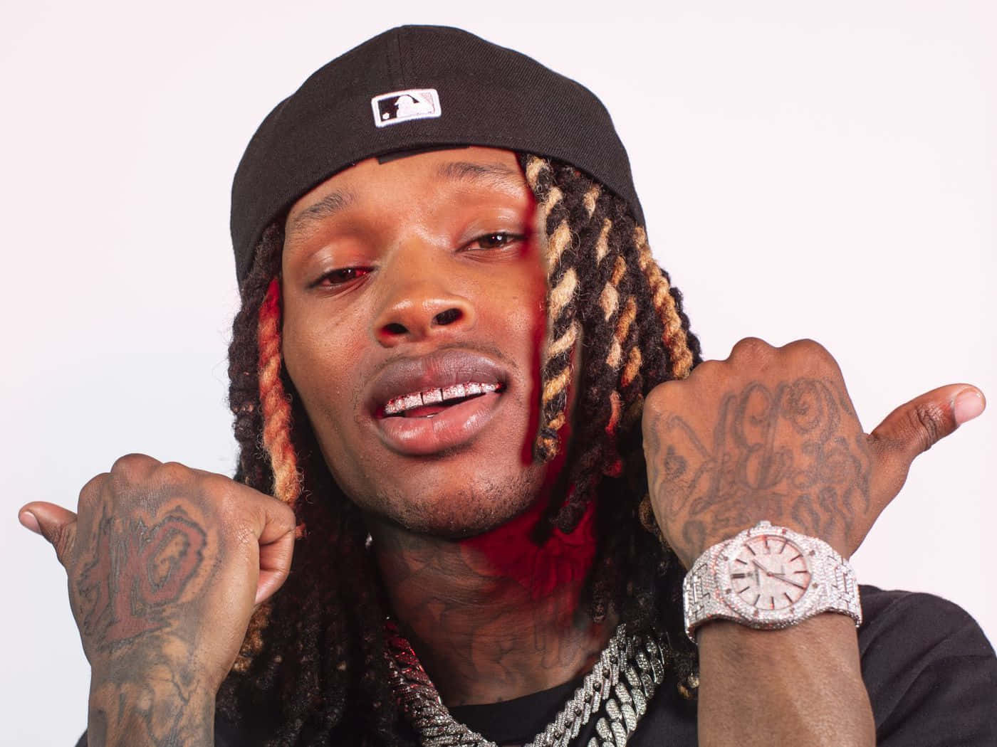 辮子頭髮和刺青的男子戴著帽子和鑽石手錶指著自己。 — King Von 壁紙