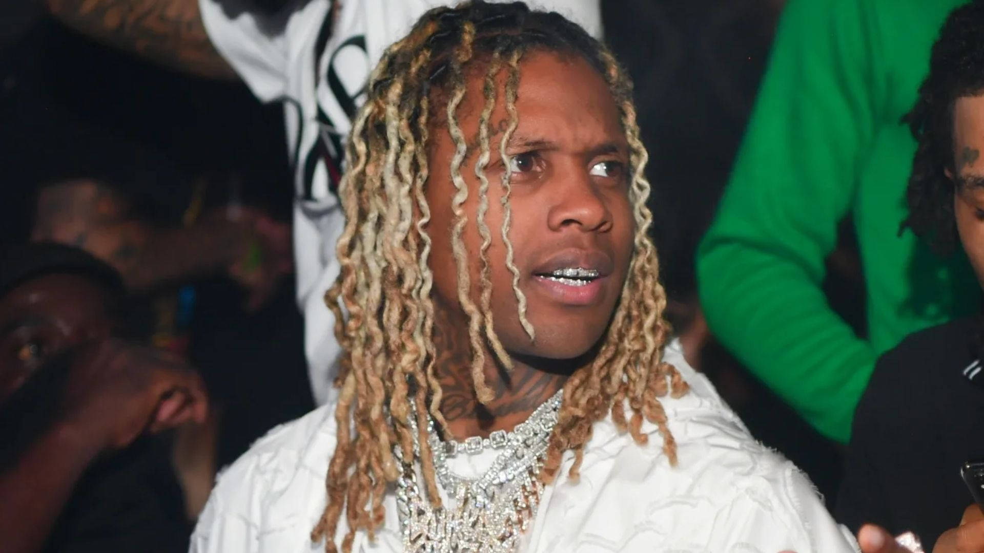 Lil Durk 桌布 壁紙 — 一名留著金色長髮辮、戴著鑽石鏈條的男子，在昏暗的人群中向上仰望。