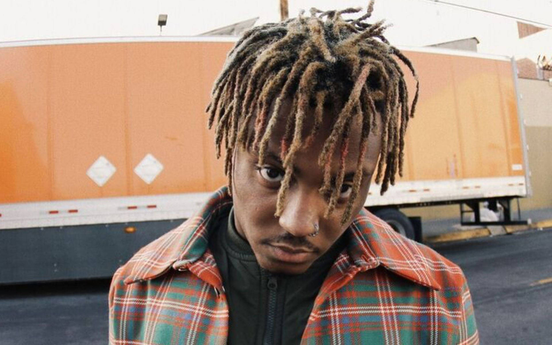 留長辮子穿格紋襯衫的年輕男子站在橙色卡車旁 — Juice Wrld 壁紙