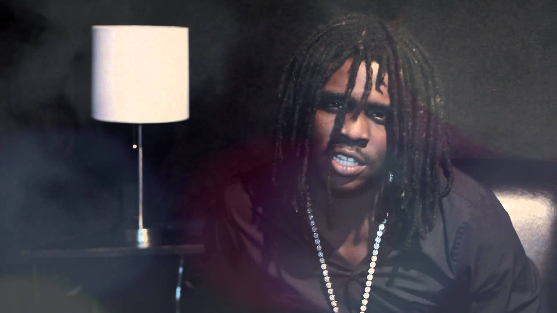 Chief Keef 桌布 壁紙 — 一名留著長髮辮的男子在昏暗的房間裡，只有一盞燈散發出柔和的光芒，他凝視著，目光強烈。