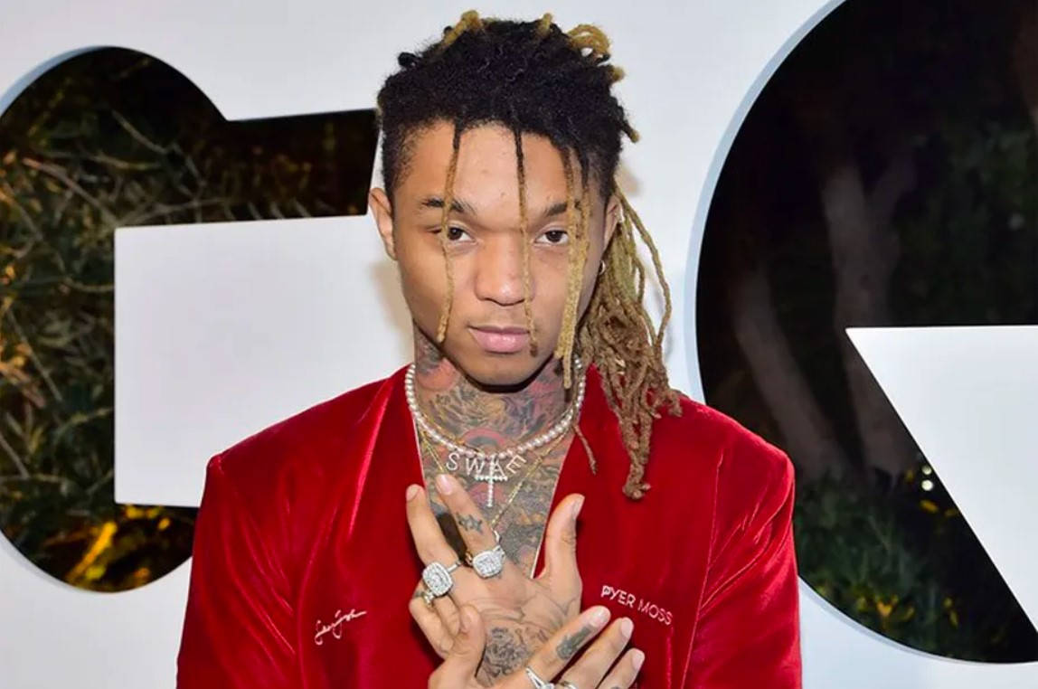 Swae Lee 桌布 壁紙 — 一名留著雷鬼辮和刺青的男子，穿著紅色天鵝絨外套並戴著多枚戒指，在活動中擺姿勢。