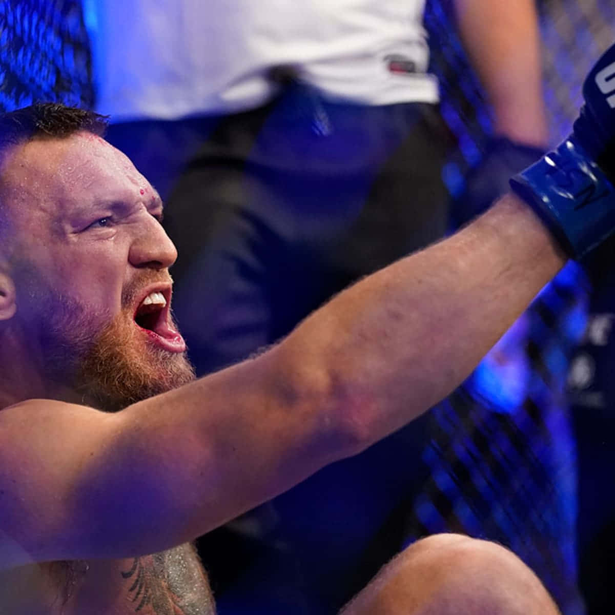 UFC 桌布 壁紙 — 一名留鬍子的戰士在藍色燈光的八角籠中勝利咆哮，高舉手臂慶祝一場殘酷比賽後的勝利。