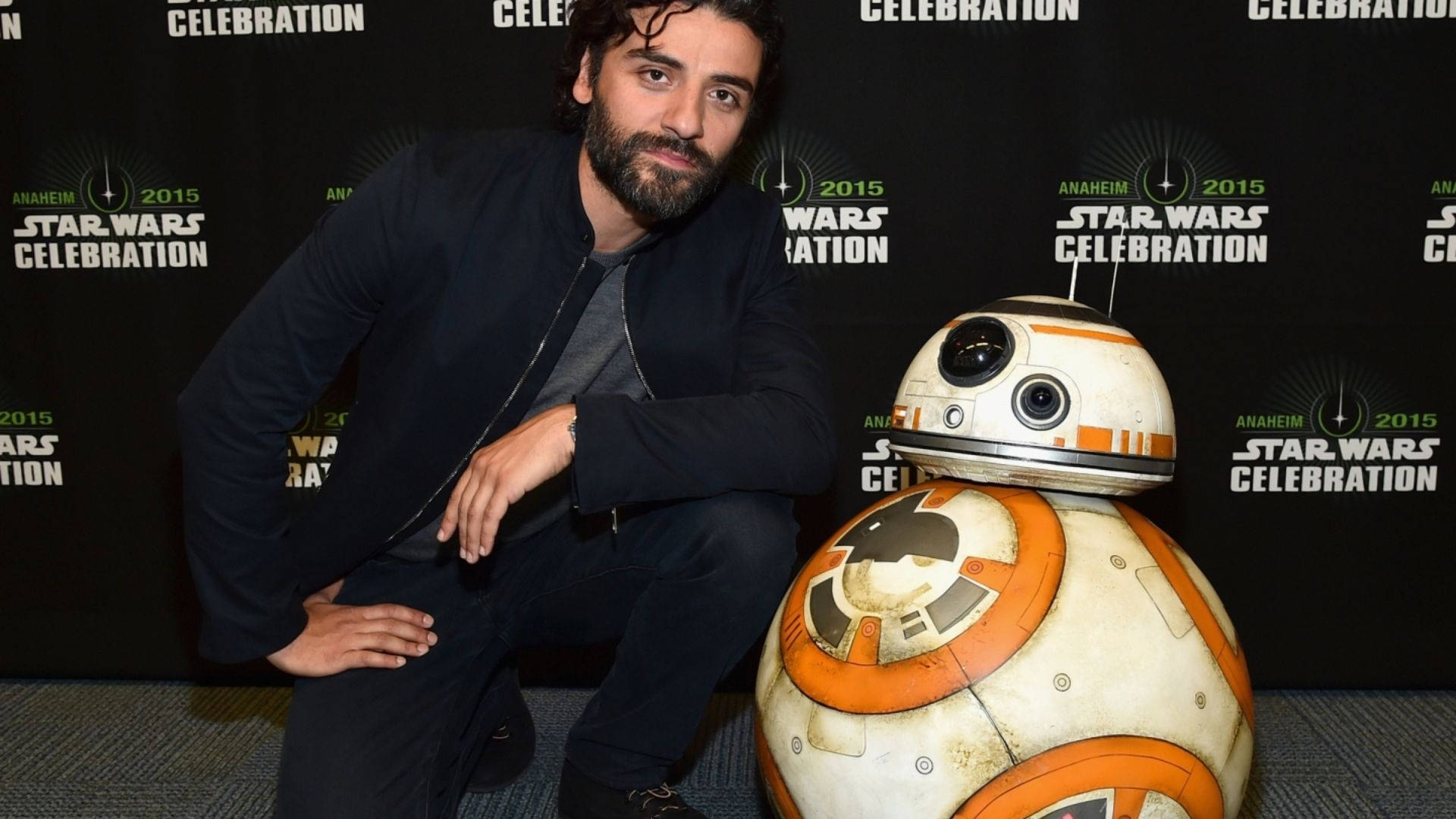 oscar 桌布 壁紙 — 一名留鬍子的男人蹲在BB-8機器人旁邊，背景是星戰慶典活動。