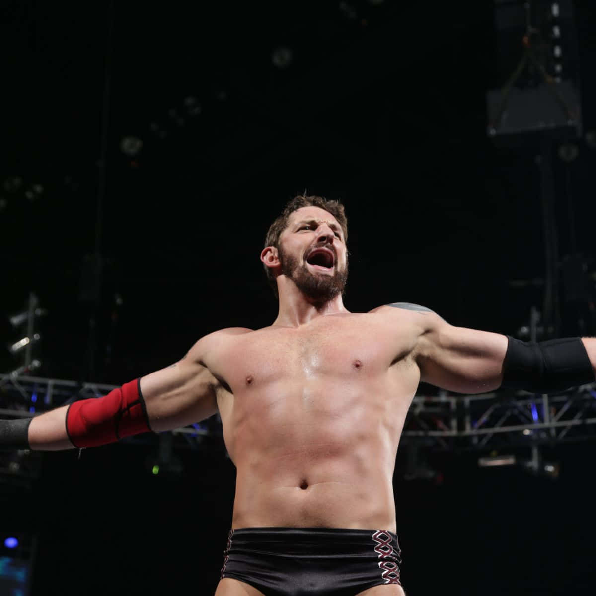 WWE 桌布 壁紙 — 一名留鬍子的肌肉摔角手在競技場燈光下張開雙臂勝利地吶喊。