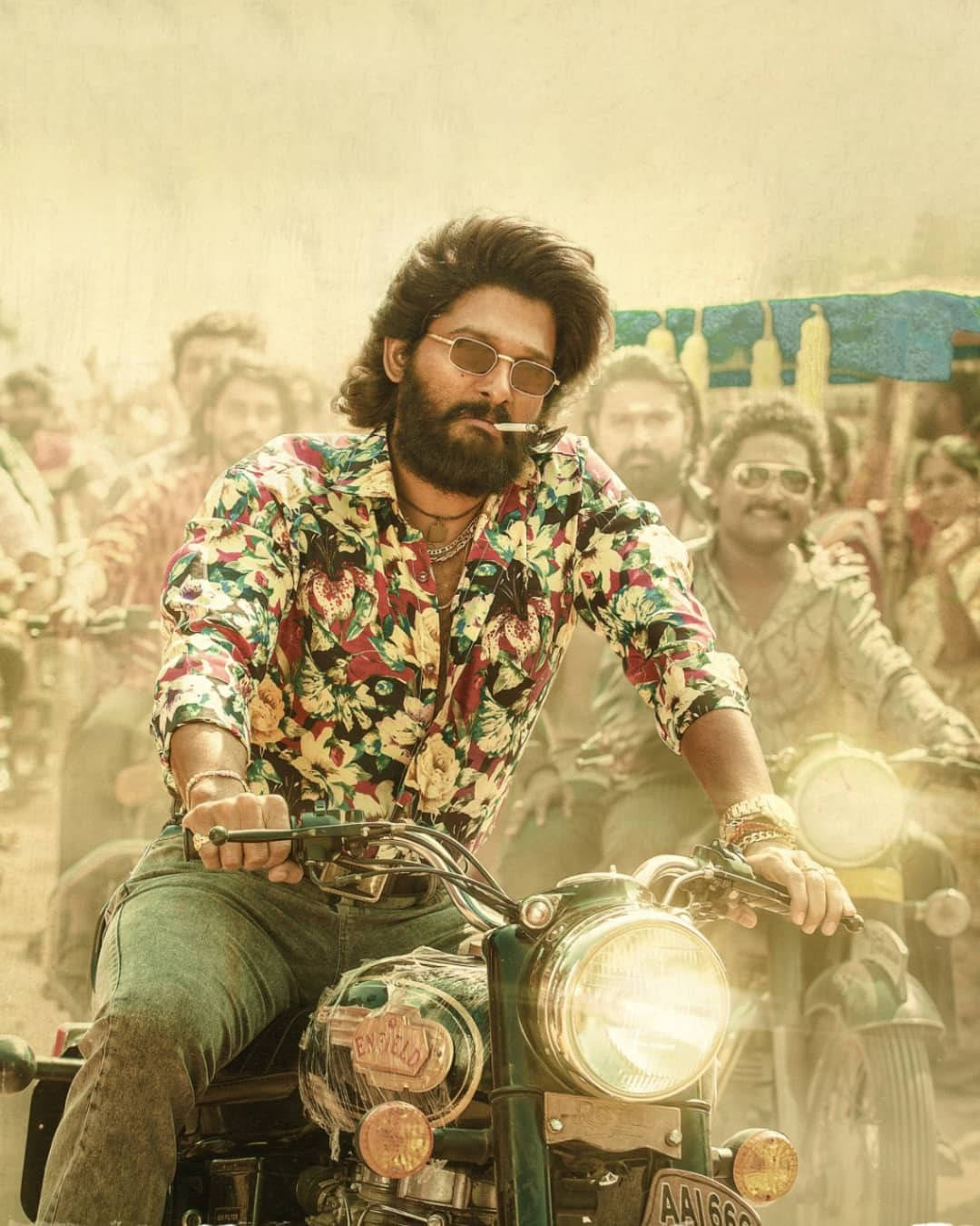 Allu Arjun 桌布 壁紙 — 一名留鬍鬚、戴太陽眼鏡的男子，穿著色彩繽紛的花襯衫，騎著復古機車穿過塵土飛揚的人群。