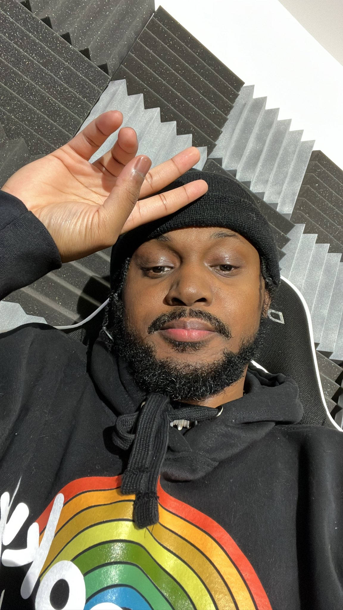 Coryxkenshin 桌布 壁紙 — 一名留鬍鬚、戴黑色毛帽的男子在一個設有隔音板的房間內，穿著帶有彩虹圖案的連帽上衣擺姿勢。