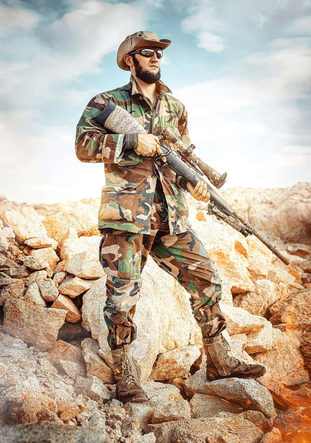 soldier 桌布 壁紙 — 一名留鬍鬚的士兵身穿迷彩裝備，站在岩石地形上，在明亮的天空下持步槍。