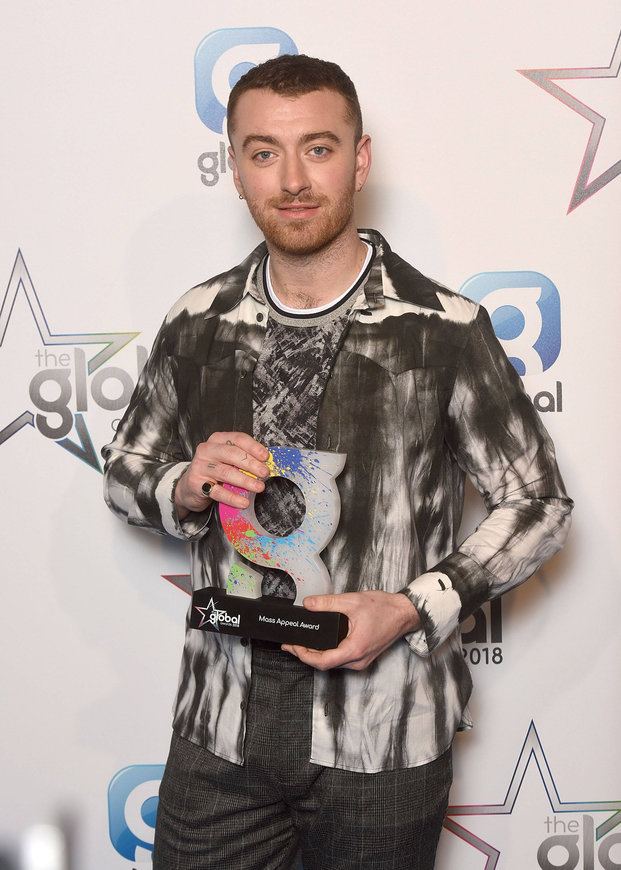 Sam Smith 桌布 壁紙 — 一名留鬍鬚的男子在Global Awards活動中，在品牌背景前手持色彩繽紛的獎項。