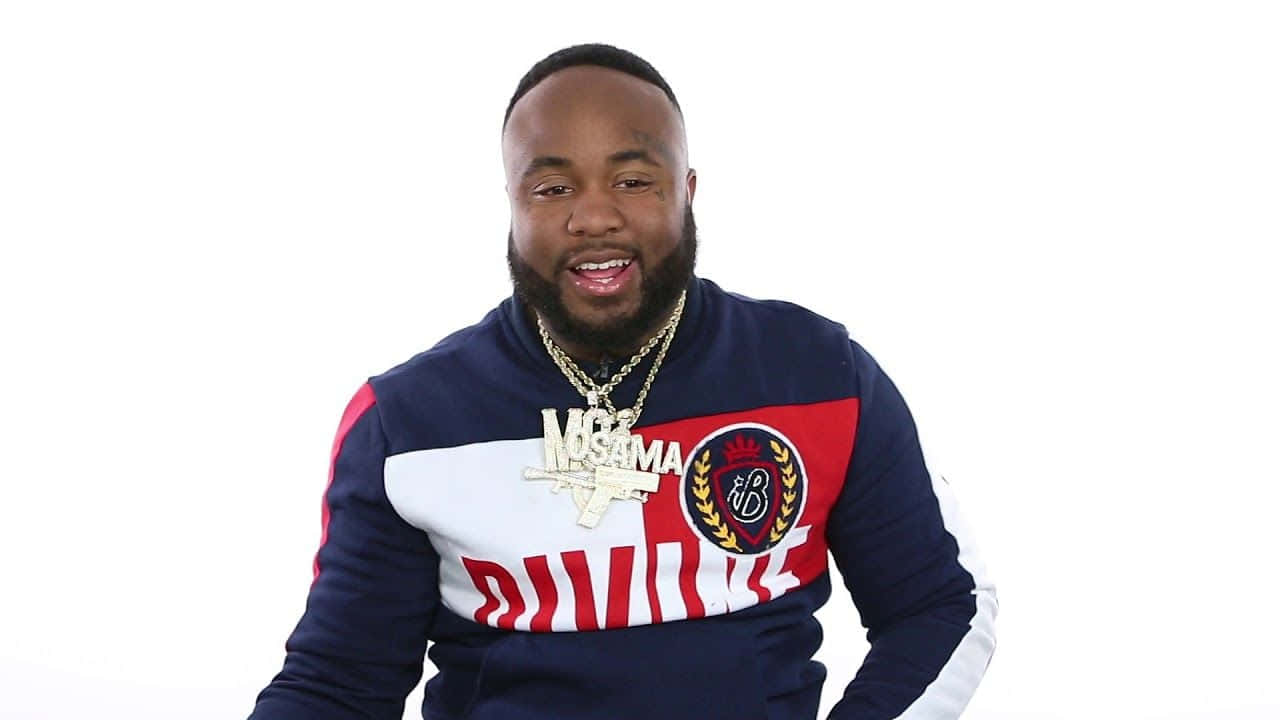 Rappers 桌布 壁紙 — 一名留鬍鬚的男子穿著一件大膽的藍、紅、白色運動衫，上面有「MOSAMA」字樣，並戴著一條手槍吊墜項鍊，背景為純白色。