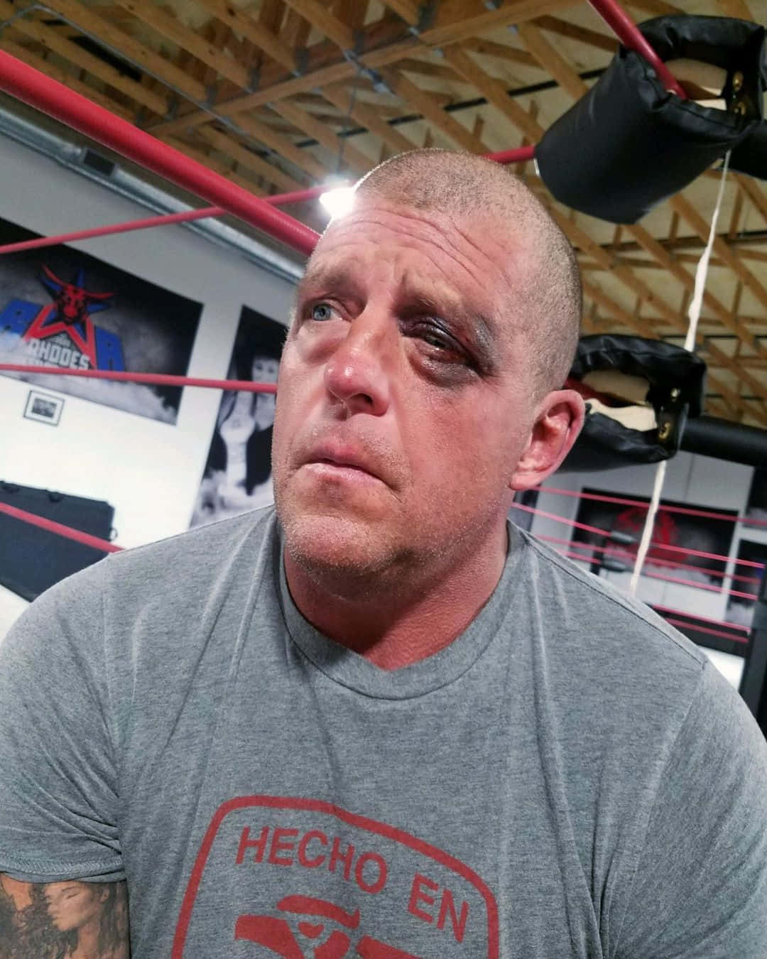 WWE 桌布 壁紙 — 一名瘀傷的摔角手，眼睛瘀青，坐在擂台上，穿著灰色T恤，上面有紅色文字。