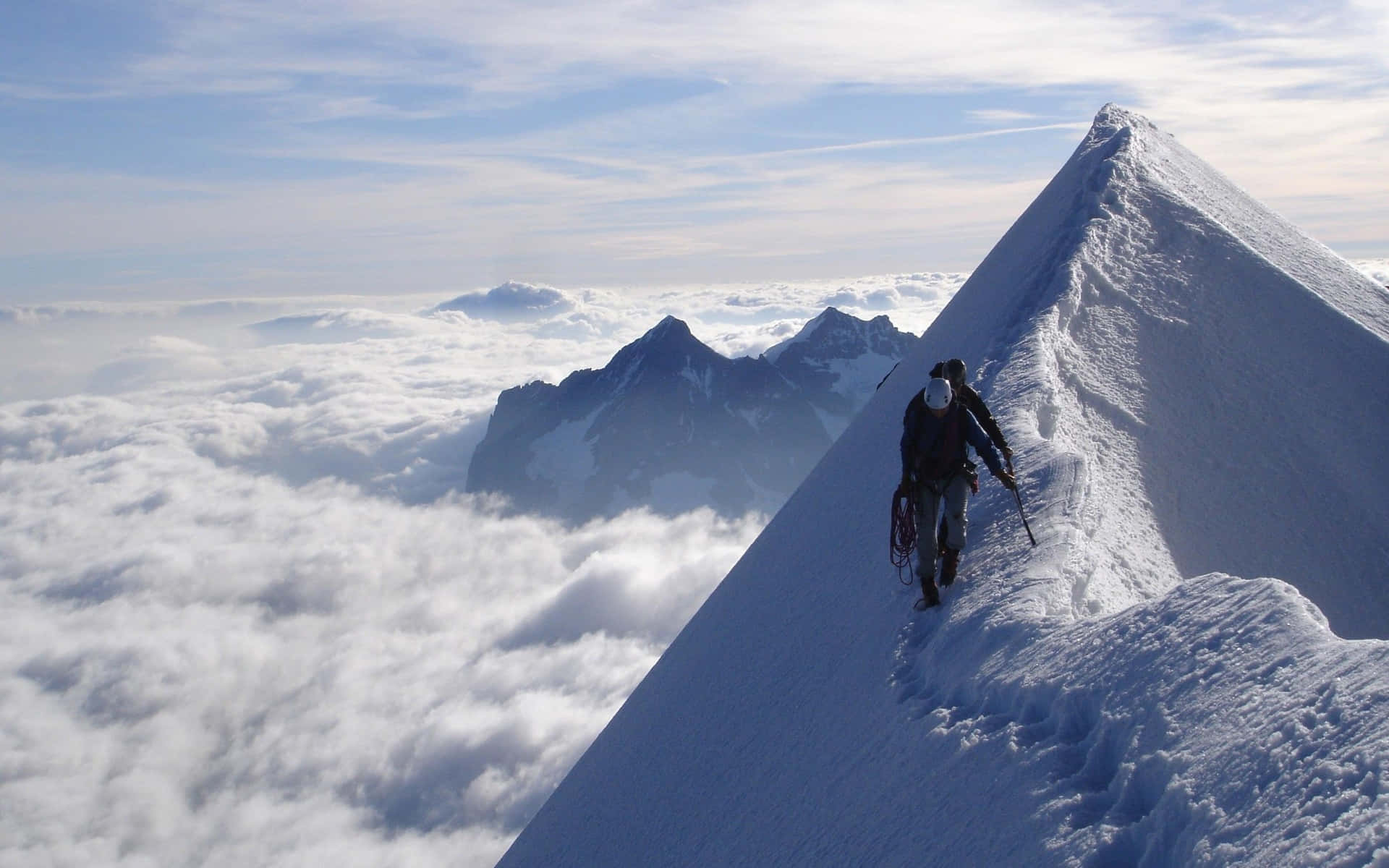 攀爬 桌布 壁紙 — 一名登山者在晴朗的藍天下，攀登雲海之上積雪覆蓋的山脊。