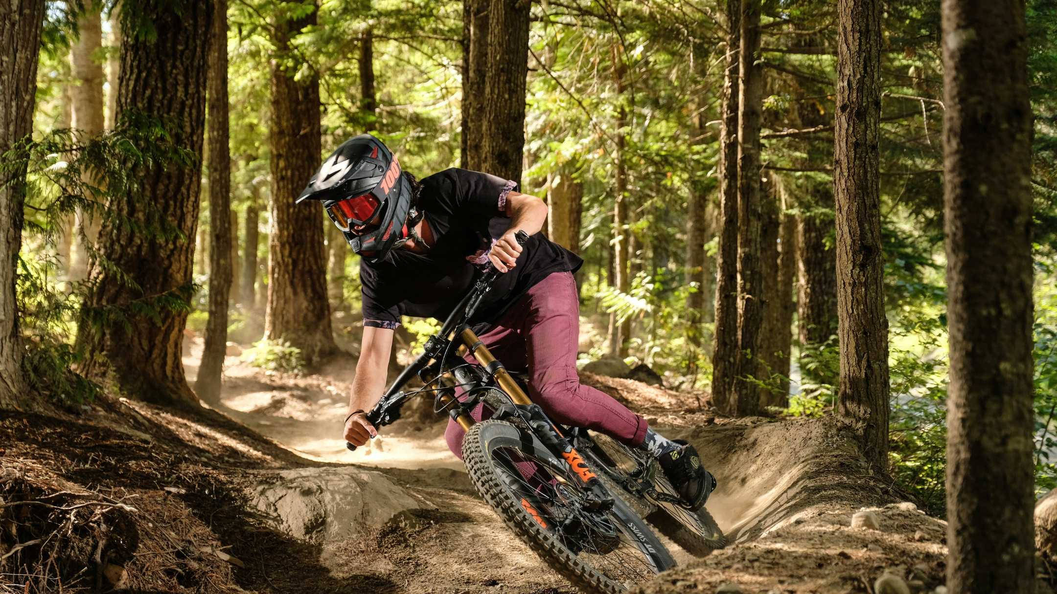 Mountain Bike 桌布 壁紙 — 一名登山自行車手在森林小徑上傾斜入一個急彎，在斑駁的陽光下揚起灰塵。