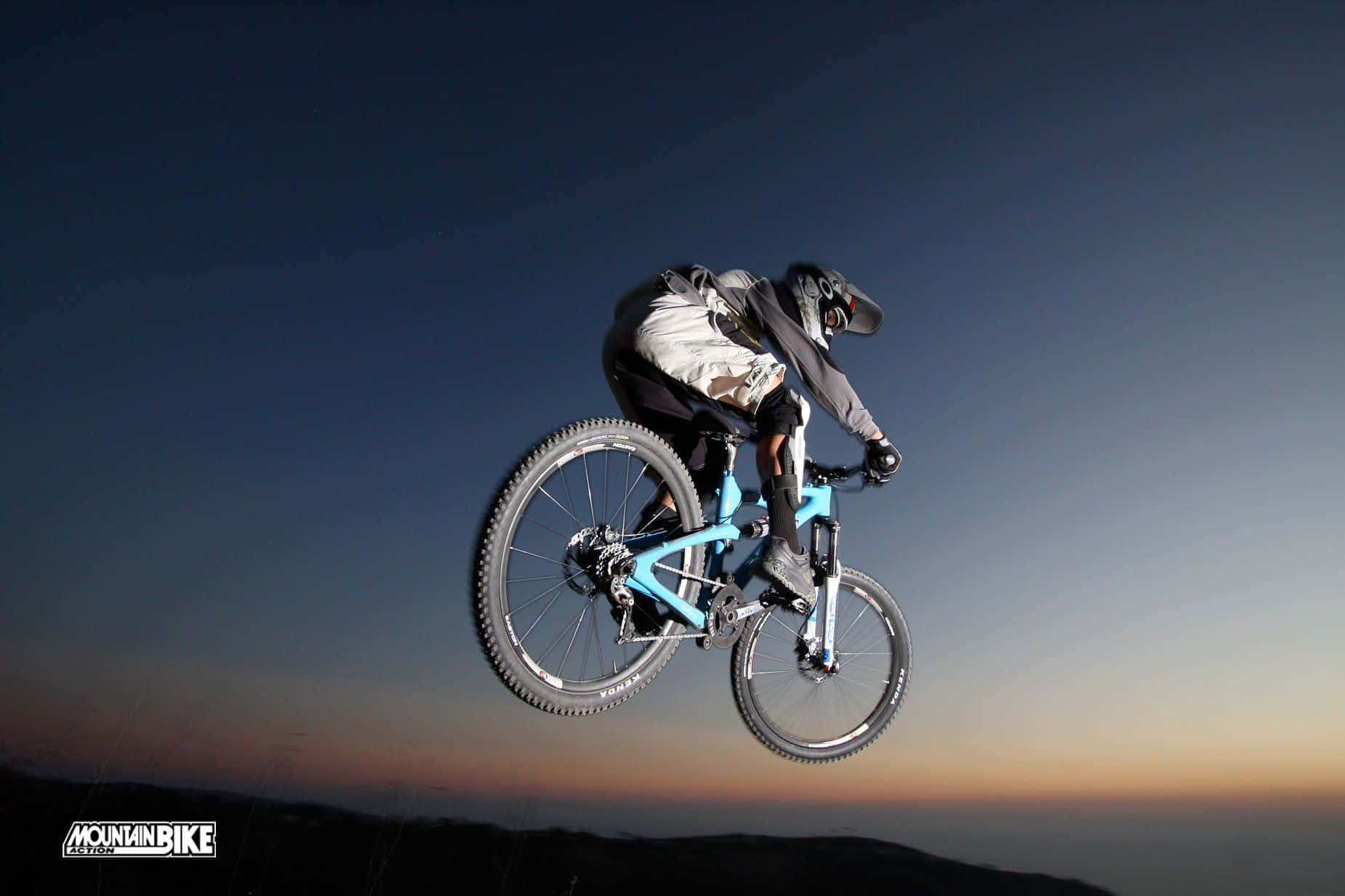 Mtb 桌布 壁紙 — 一名登山車騎士在暮色天空中翱翔，天空從深藍色漸變到下方的暖橙色。
