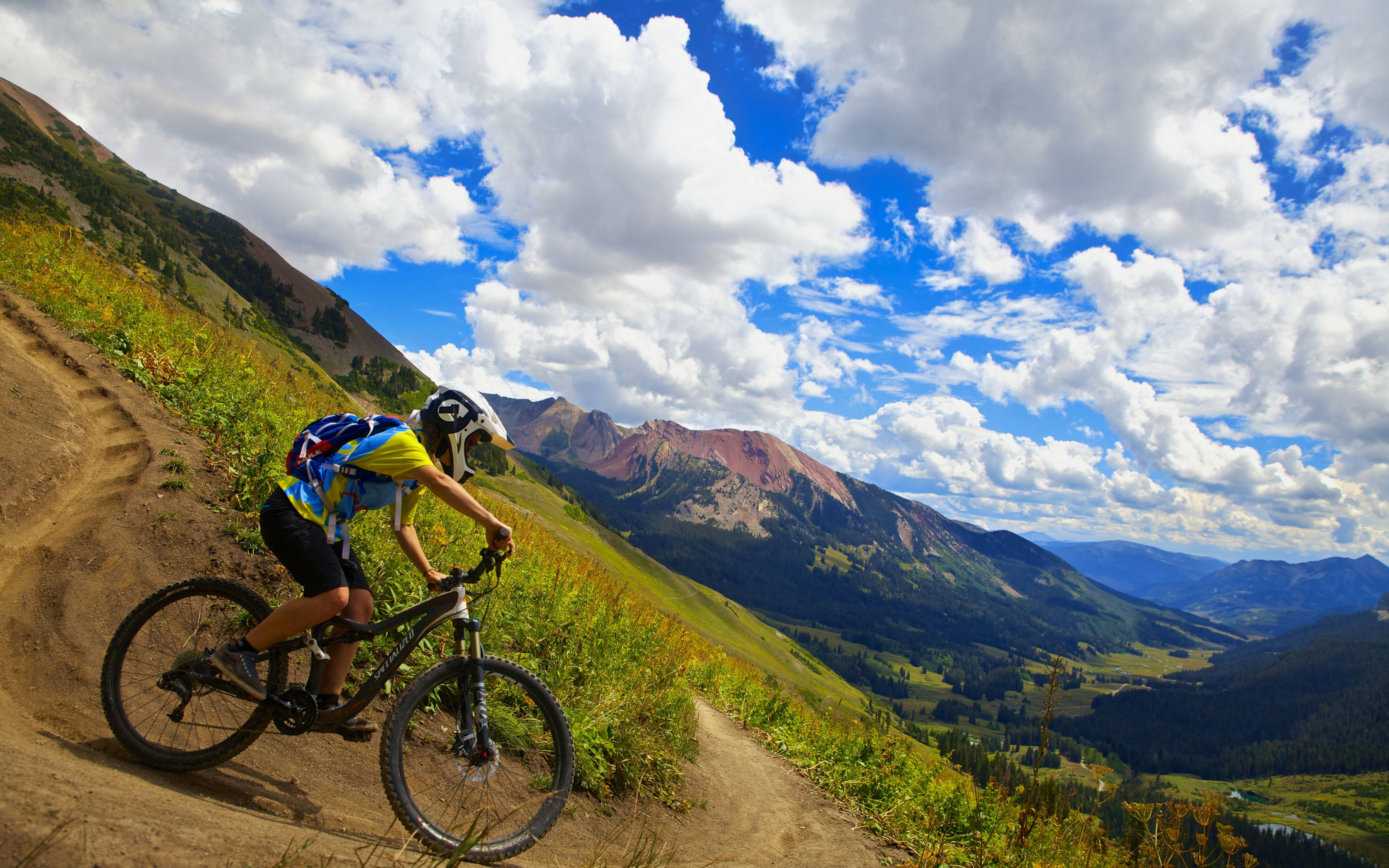 Mountain Bike 桌布 壁紙 — 一名登山車騎士在泥土小徑上傾身過彎，背景是戲劇性的雲層和崎嶇的山峰。
