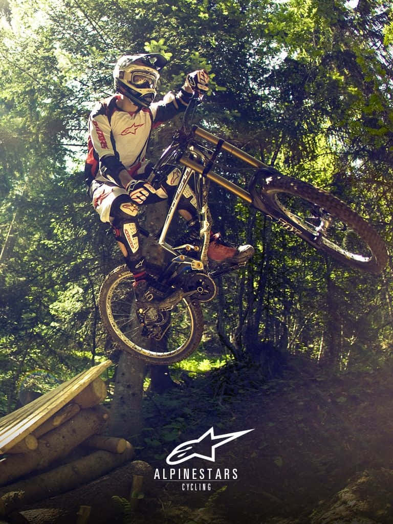 山景 桌布 壁紙 — 一名登山車騎士在陽光明媚的森林中，飛越木製跳台，戴著頭盔，專注無比。